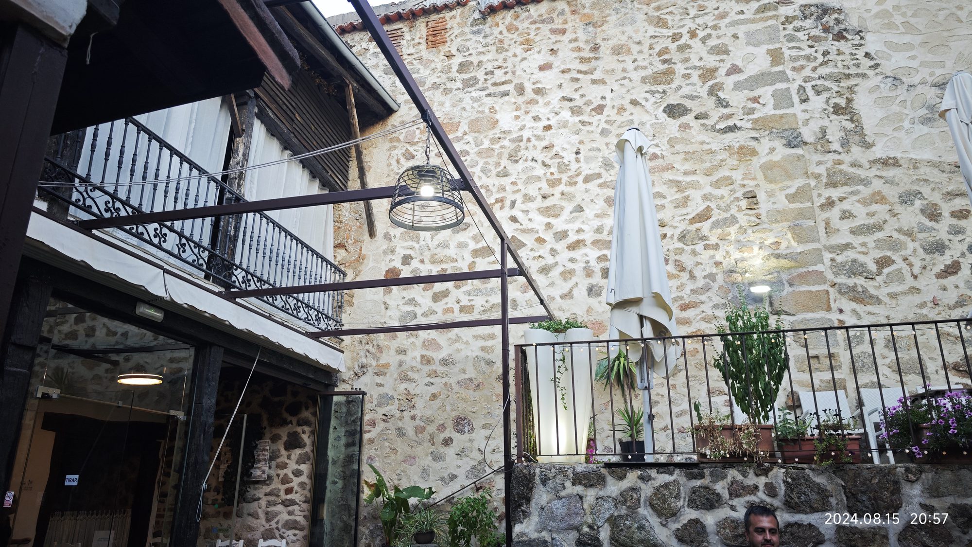 Patio interior de piedra con balcones tradicionales y terraza iluminada al anochecer.