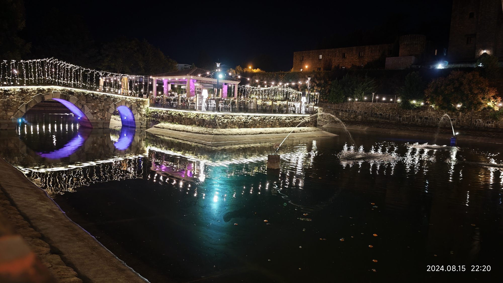 Puente de piedra iluminado de noche reflejado en el agua con luces festivas.