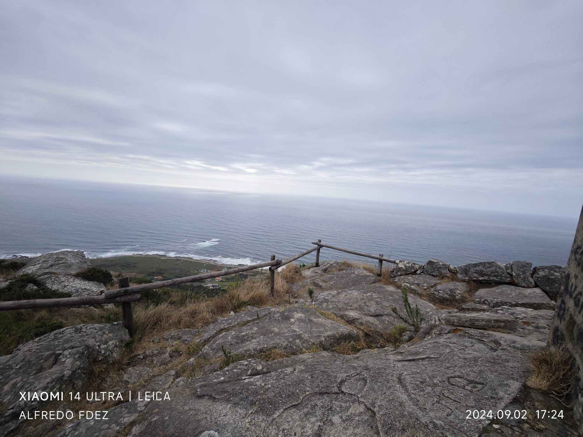 Mirador rocoso con barandilla de madera sobre el océano Atlántico en un día nublado.