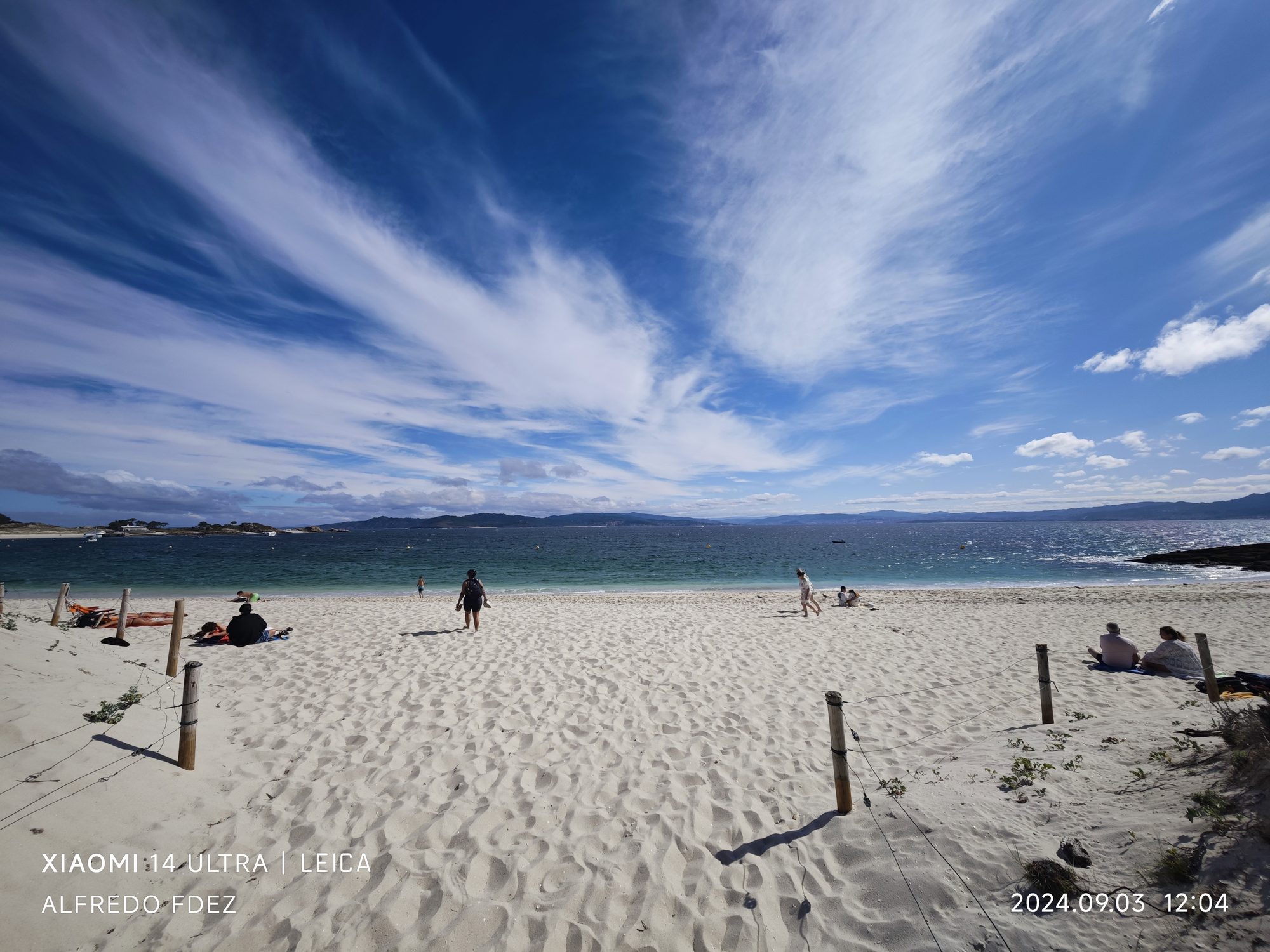 Playa de arena blanca y aguas turquesas bajo un amplio cielo azul con nubes.
