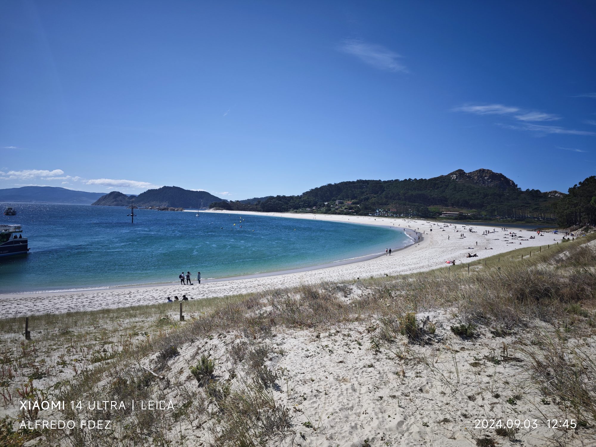 Playa de arena blanca y agua turquesa curvada entre dunas y colinas verdes.
