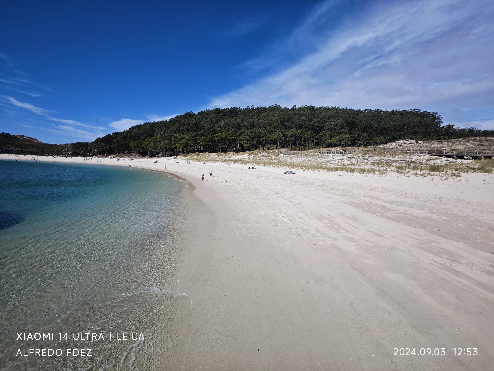 Playa de arena blanca y aguas turquesas cristalinas bordeada por un denso pinar.