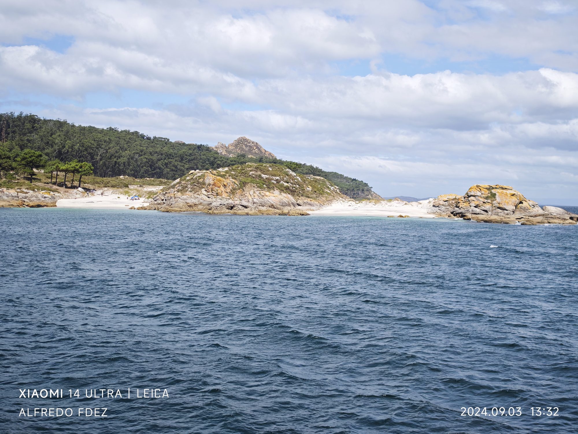 Playa de arena blanca y costa rocosa con frondosas colinas verdes en Vigo.
