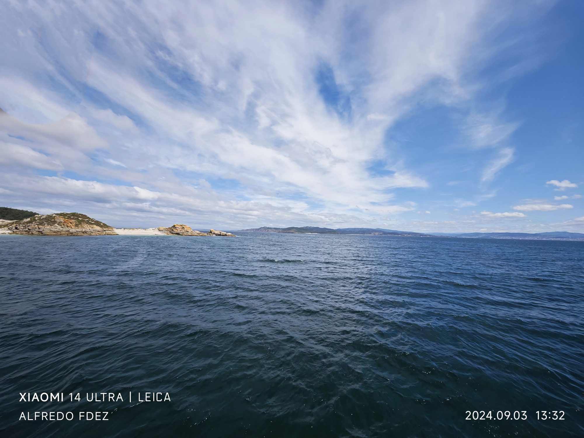 Aguas azules de la ría de Vigo bajo un cielo despejado con nubes dispersas.