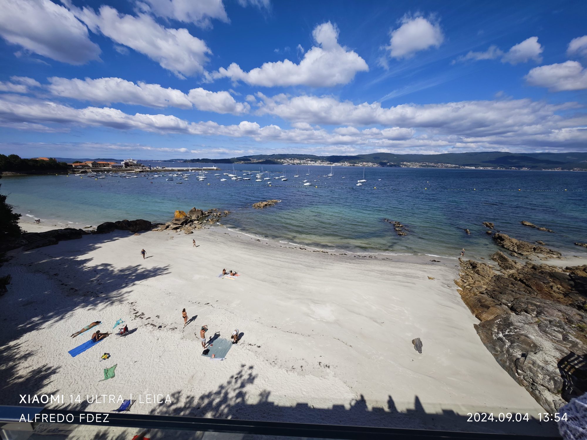 Playa de arena blanca y agua turquesa con barcos fondeados en la costa de Marín.
