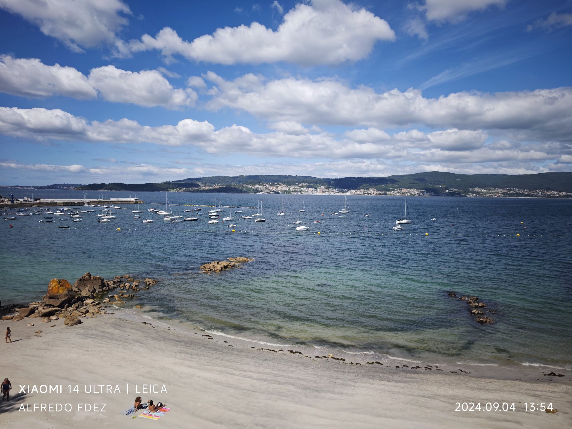 Playa de arena y aguas turquesas con barcos fondeados en la ría de Marín.