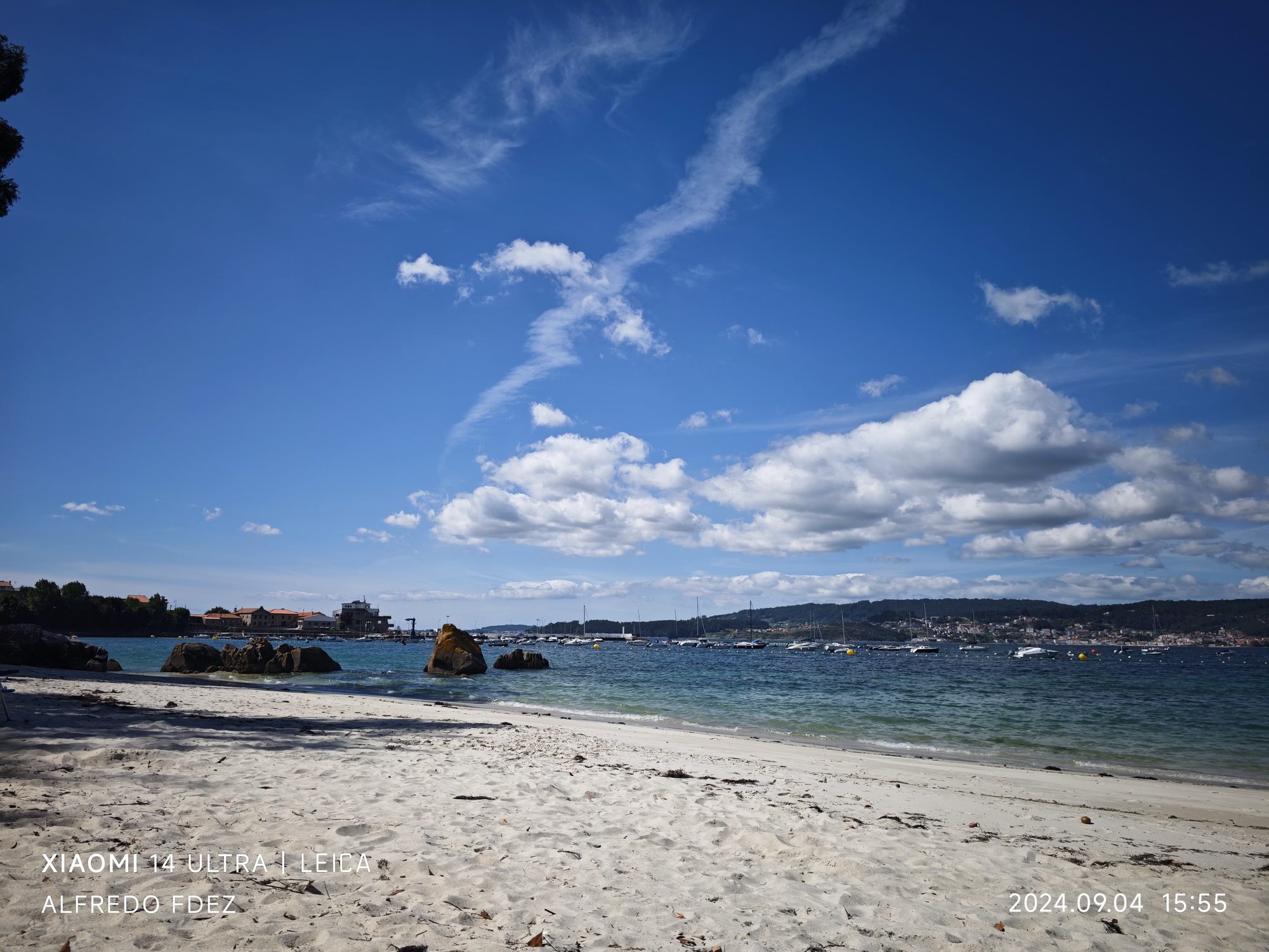 Playa de arena clara, aguas turquesas y rocas bajo un cielo azul con nubes.