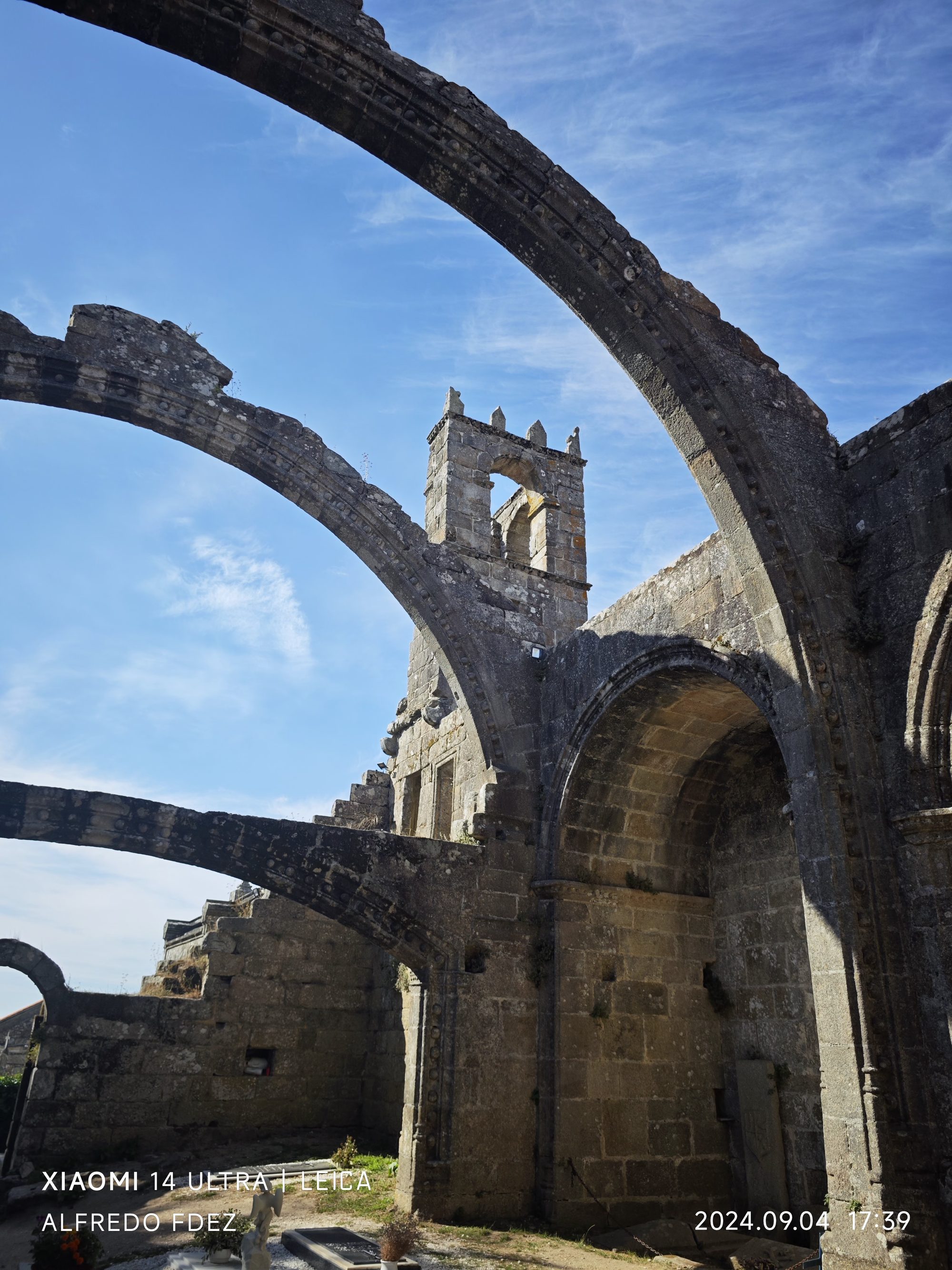 Arcos góticos de piedra y campanario de ruinas históricas bajo el cielo azul.