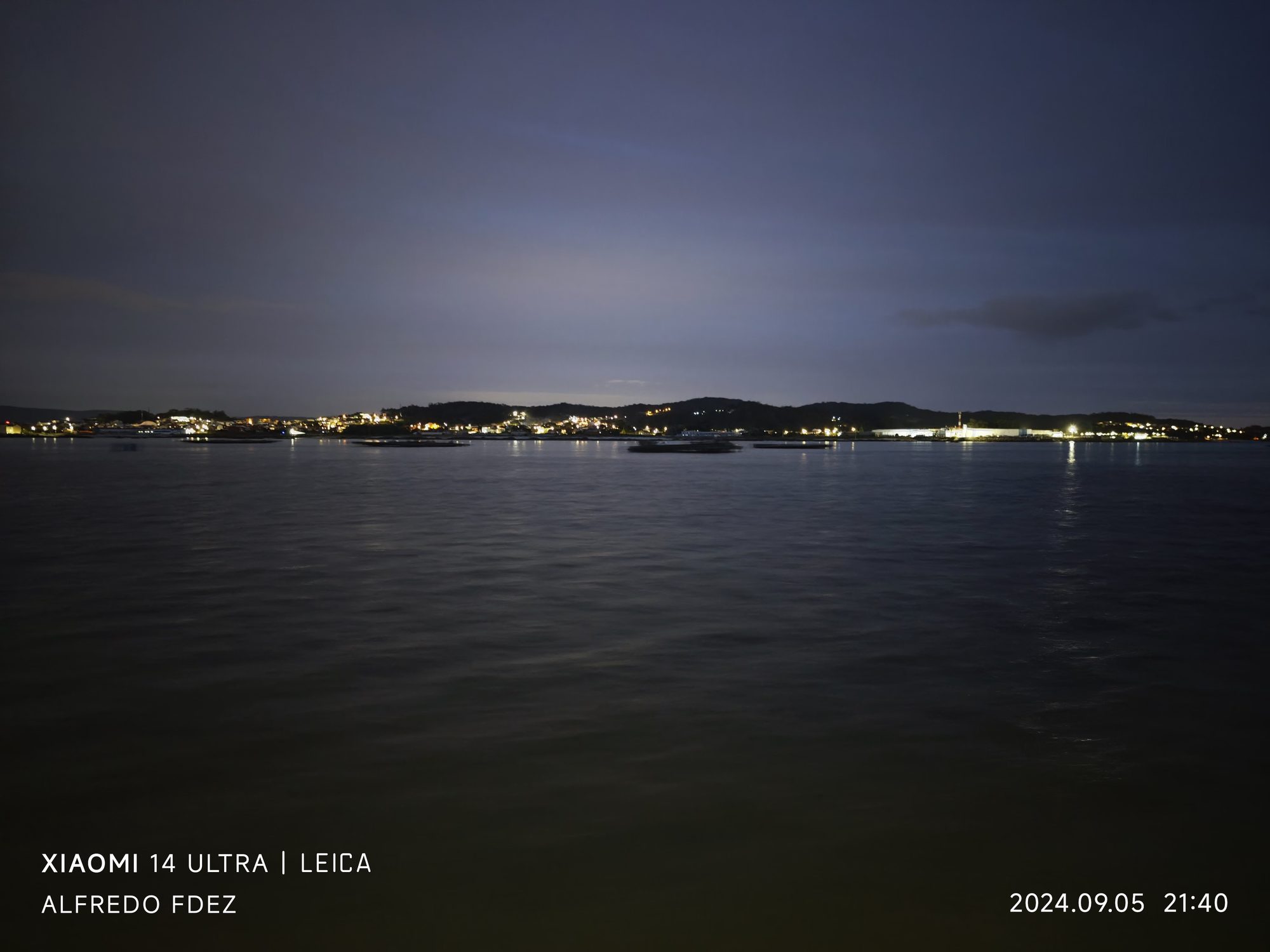 Vista nocturna del mar con las luces lejanas de la costa en el horizonte.