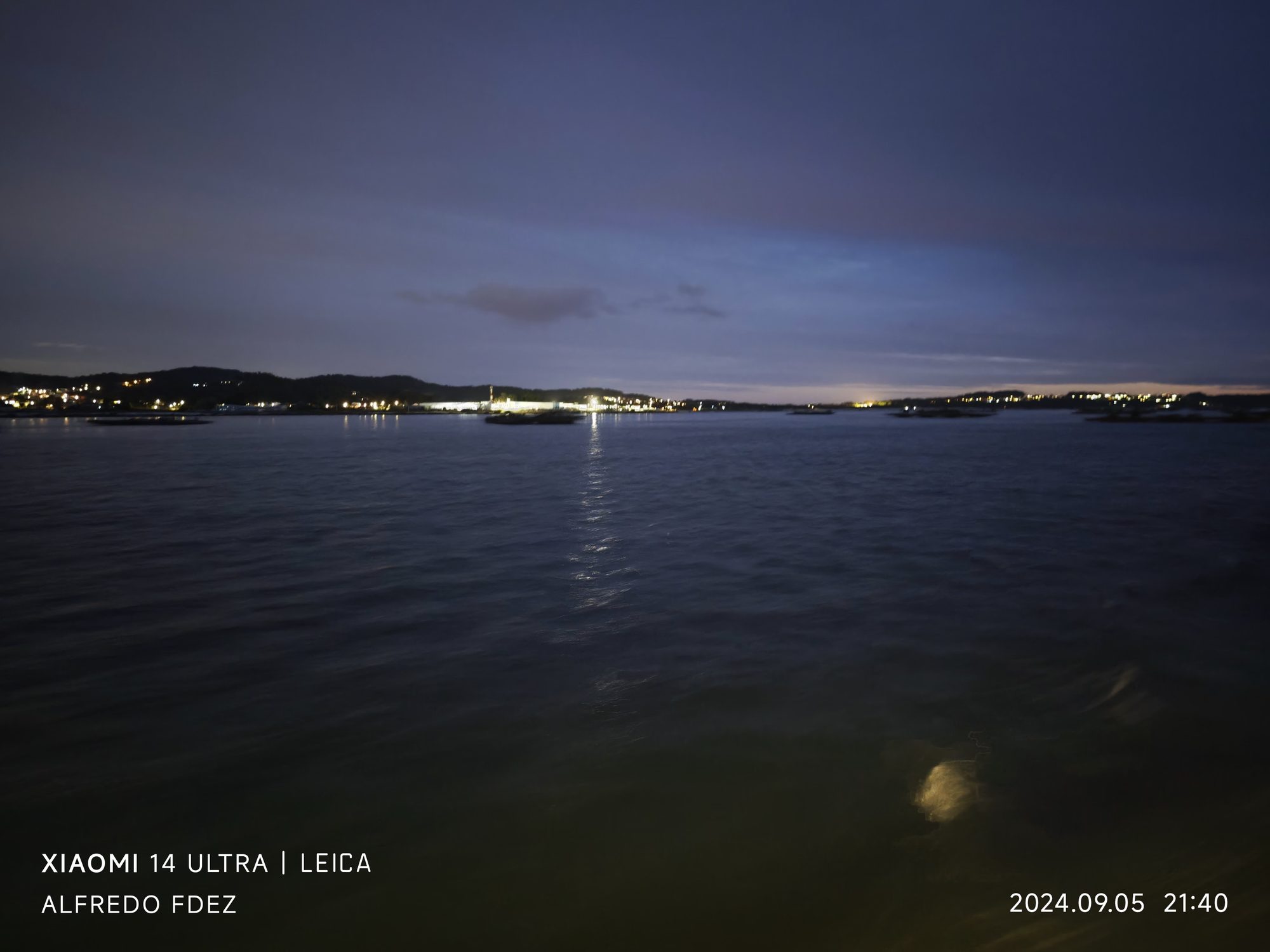 Vista nocturna sobre el agua con luces reflejadas en la costa de O Grove.
