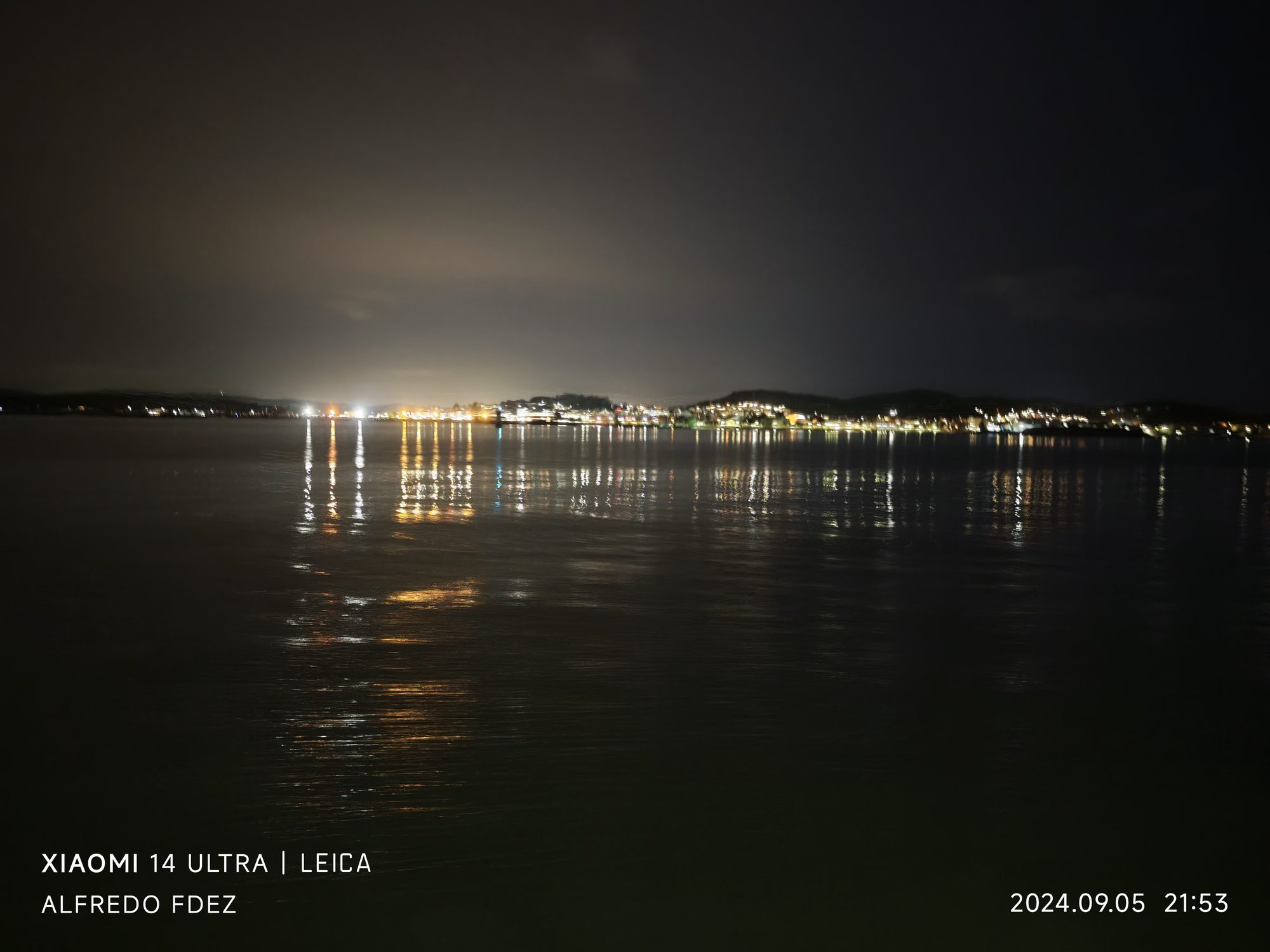 Luces nocturnas de la costa y sus reflejos dorados sobre el agua tranquila del mar.