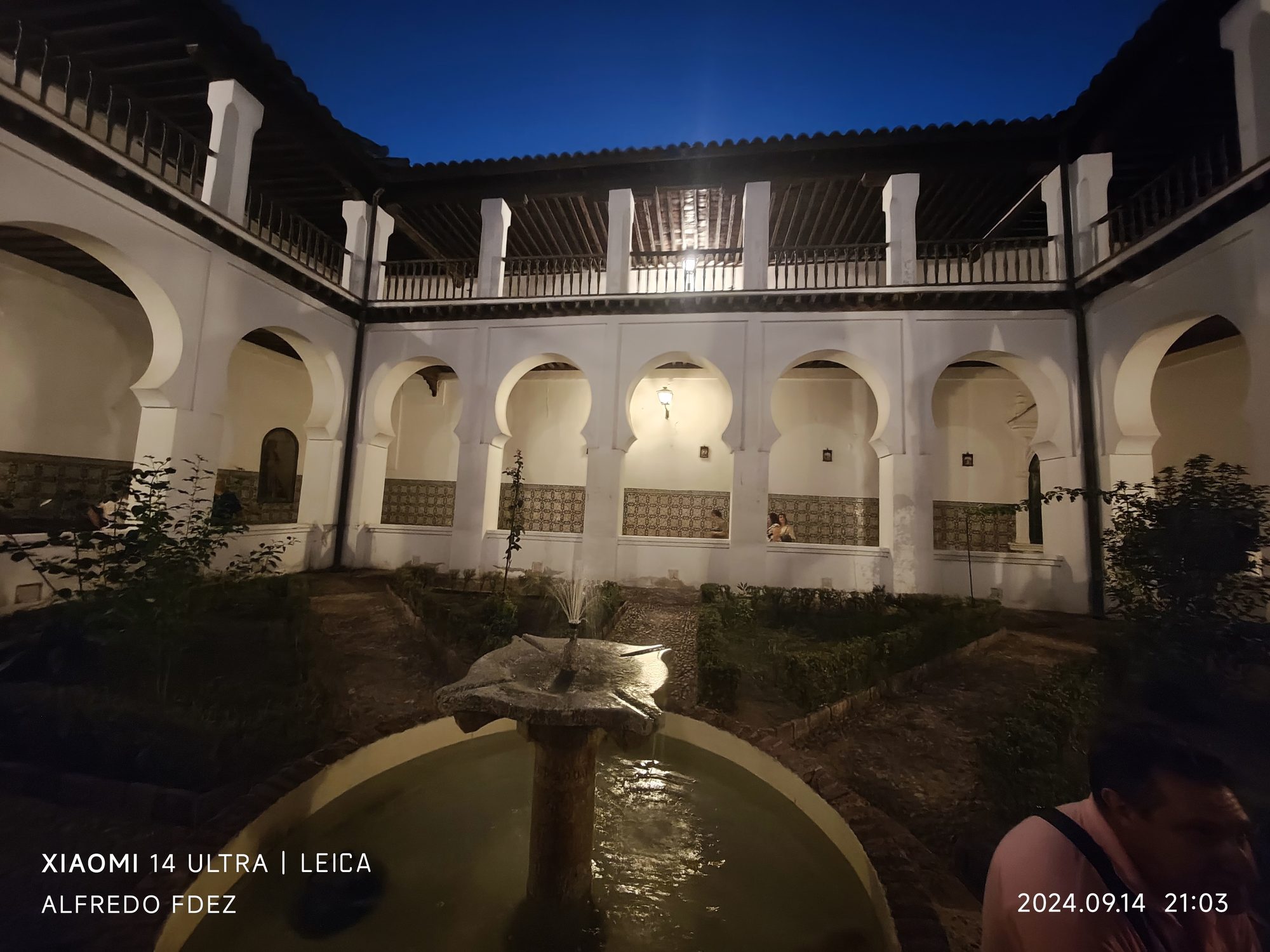 Patio interior de estilo mudéjar iluminado de noche con fuente central.