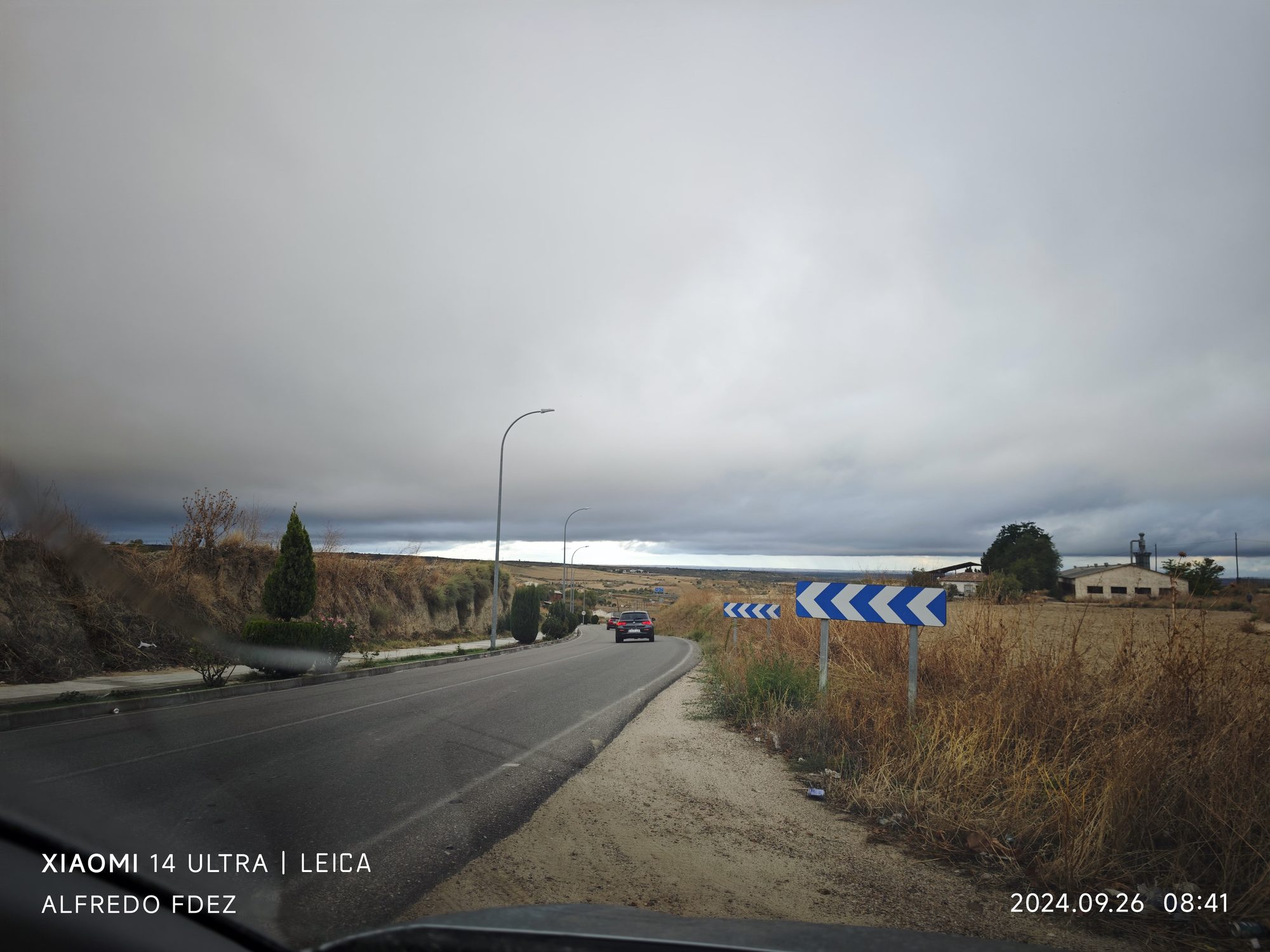Carretera con curvas y señales de tráfico bajo un cielo gris nublado en el campo.