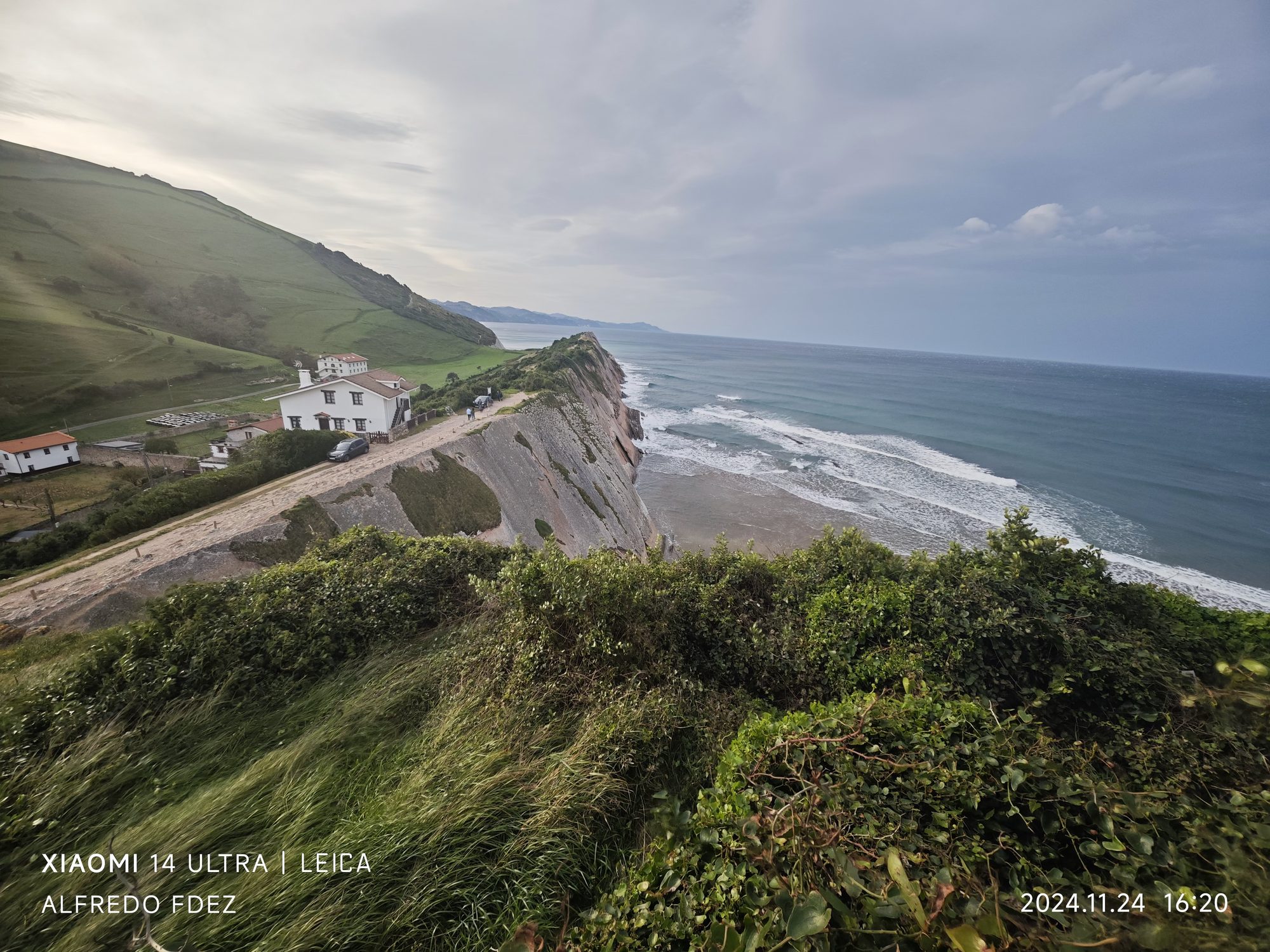 Acantilados verdes de Zumaia descendiendo hacia el mar Cantábrico bajo un cielo nublado.