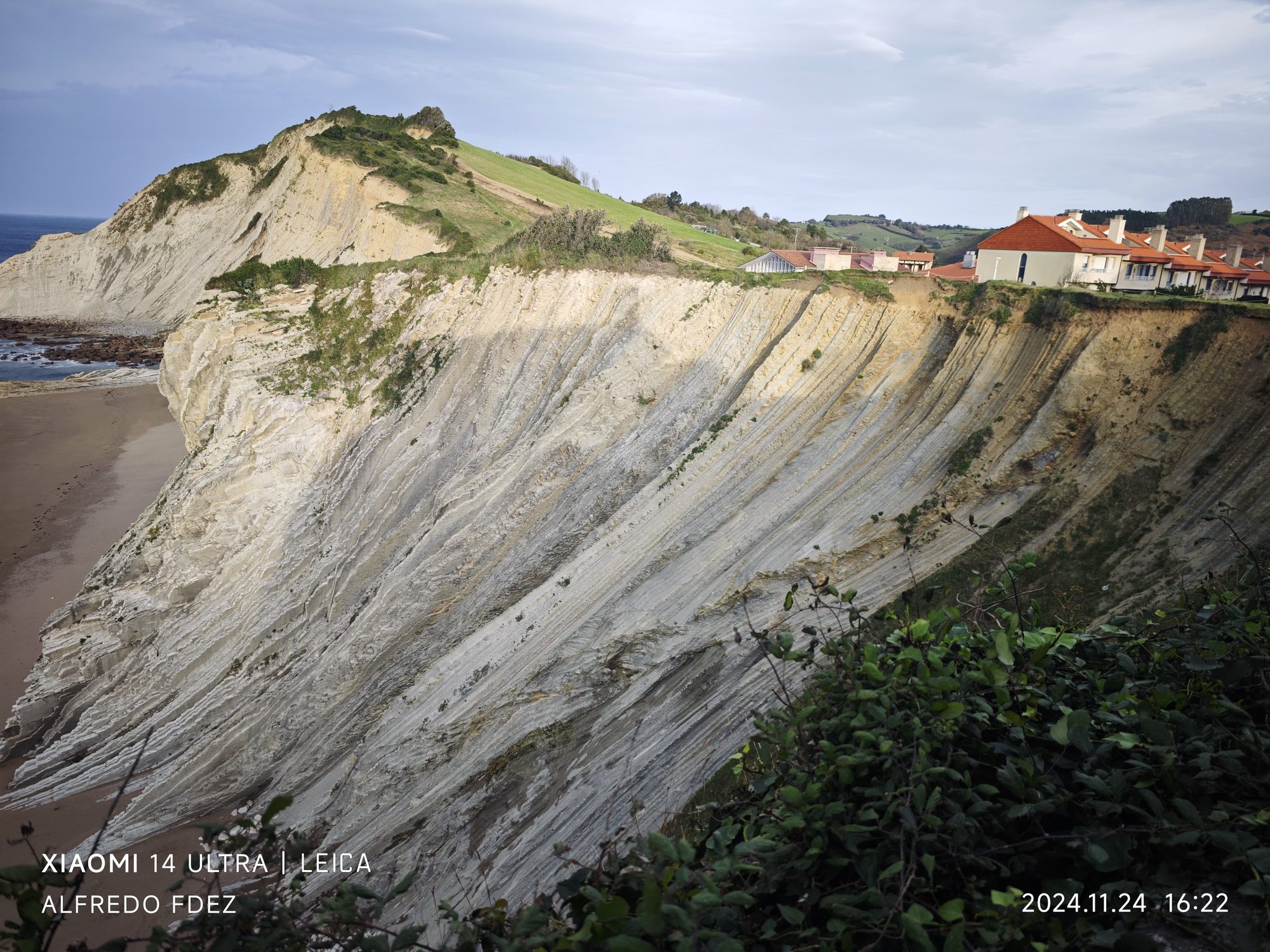 Impresionantes acantilados de flysch estratificado sobre la playa con casas en la cumbre en Zumaia.