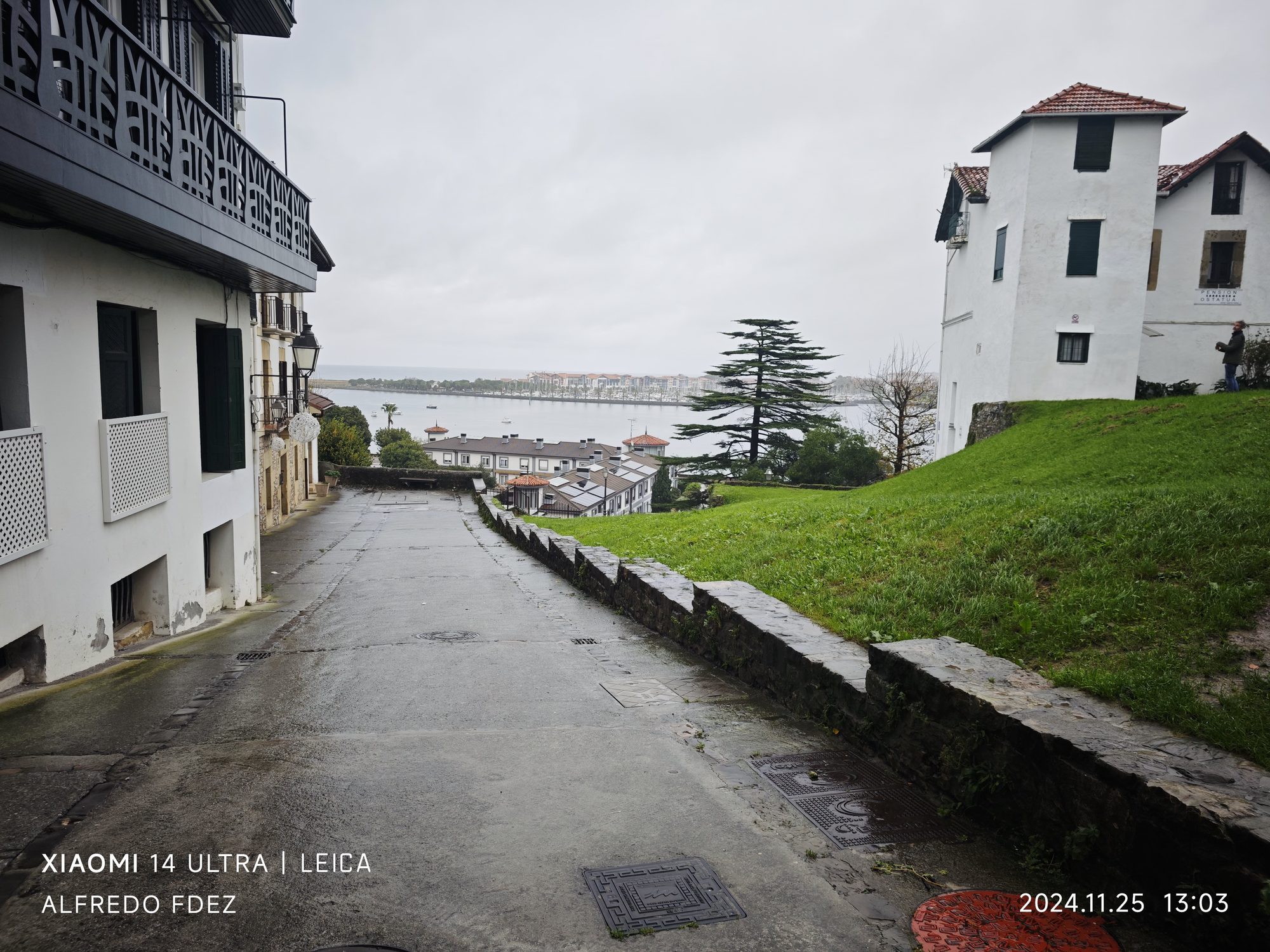 Calle empedrada mojada descendiendo hacia la bahía entre casas blancas en Fuenterrabía.