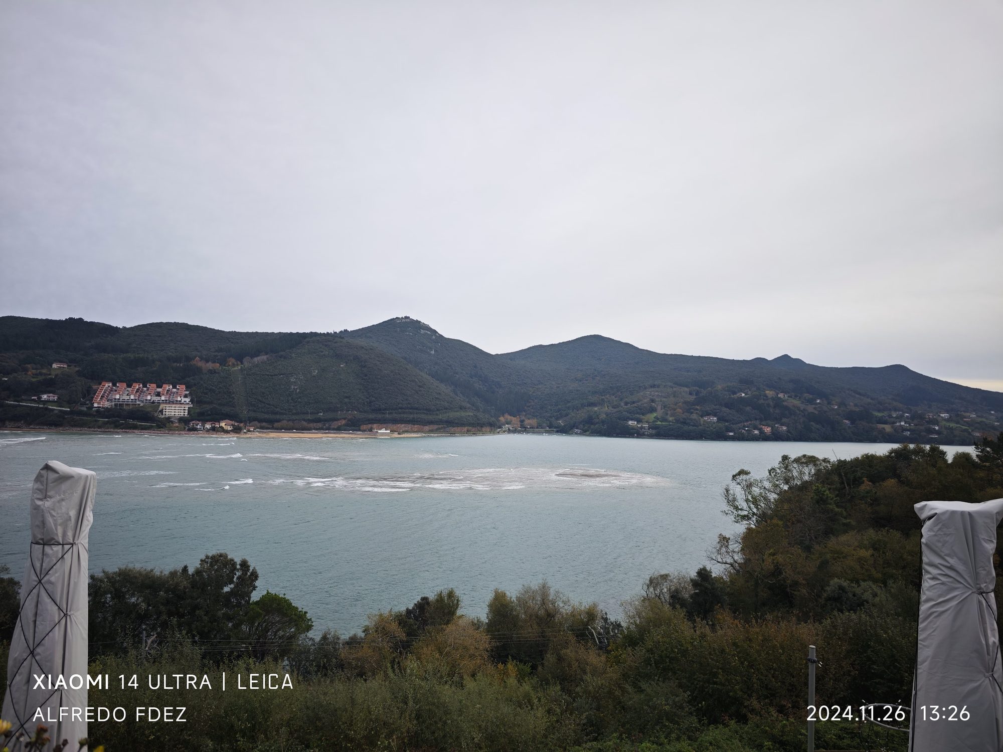 Vista panorámica de la ría de Mundaca rodeada de montes verdes bajo cielo nublado.