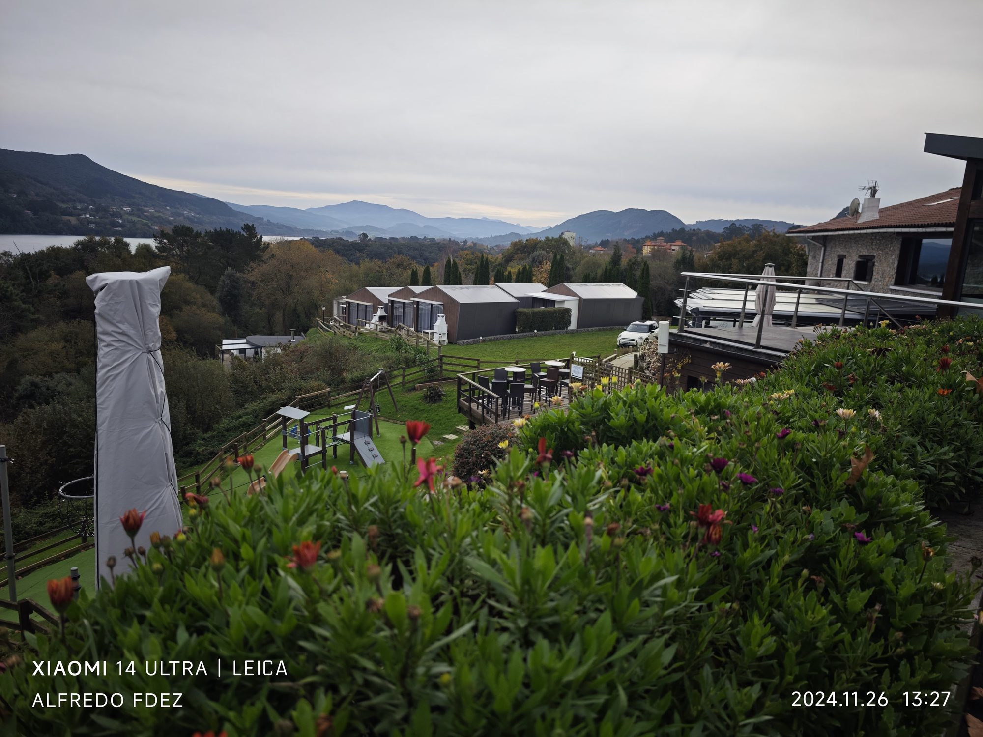 Vista panorámica de cabañas modernas entre colinas verdes y montañas frente a la ría.