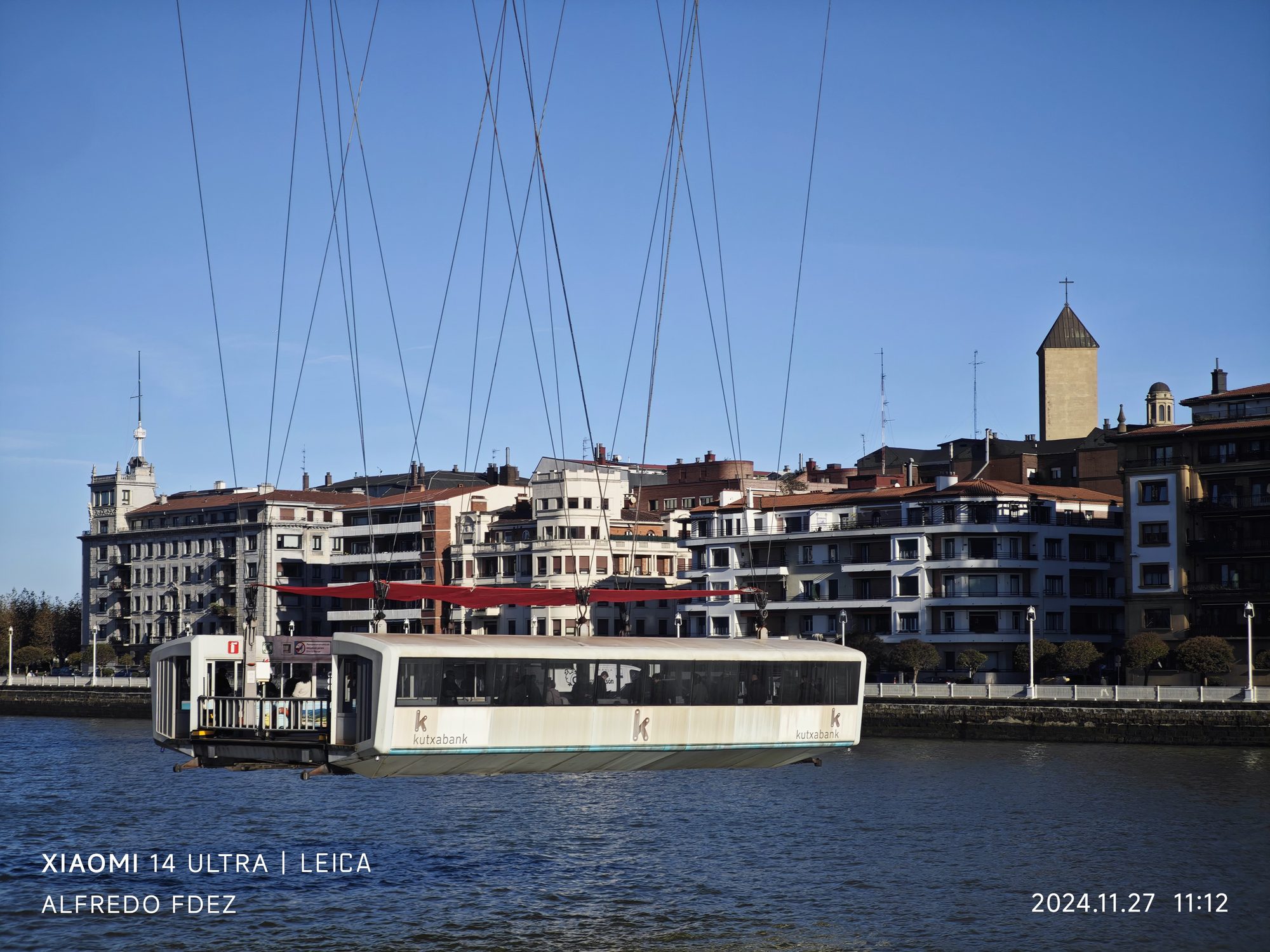 Barquilla suspendida del Puente Colgante cruzando la ría con edificios de Portugalete al fondo.