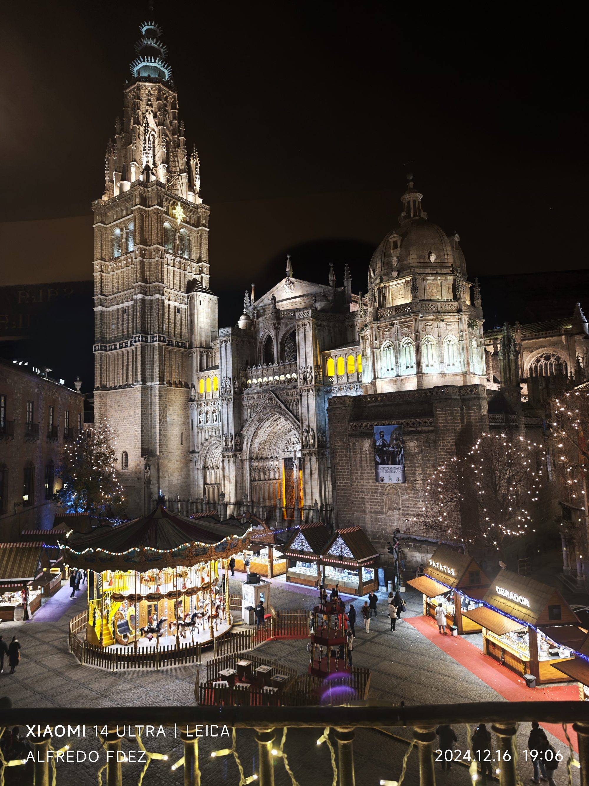 Catedral de Toledo iluminada de noche junto a un mercado navideño y un carrusel.