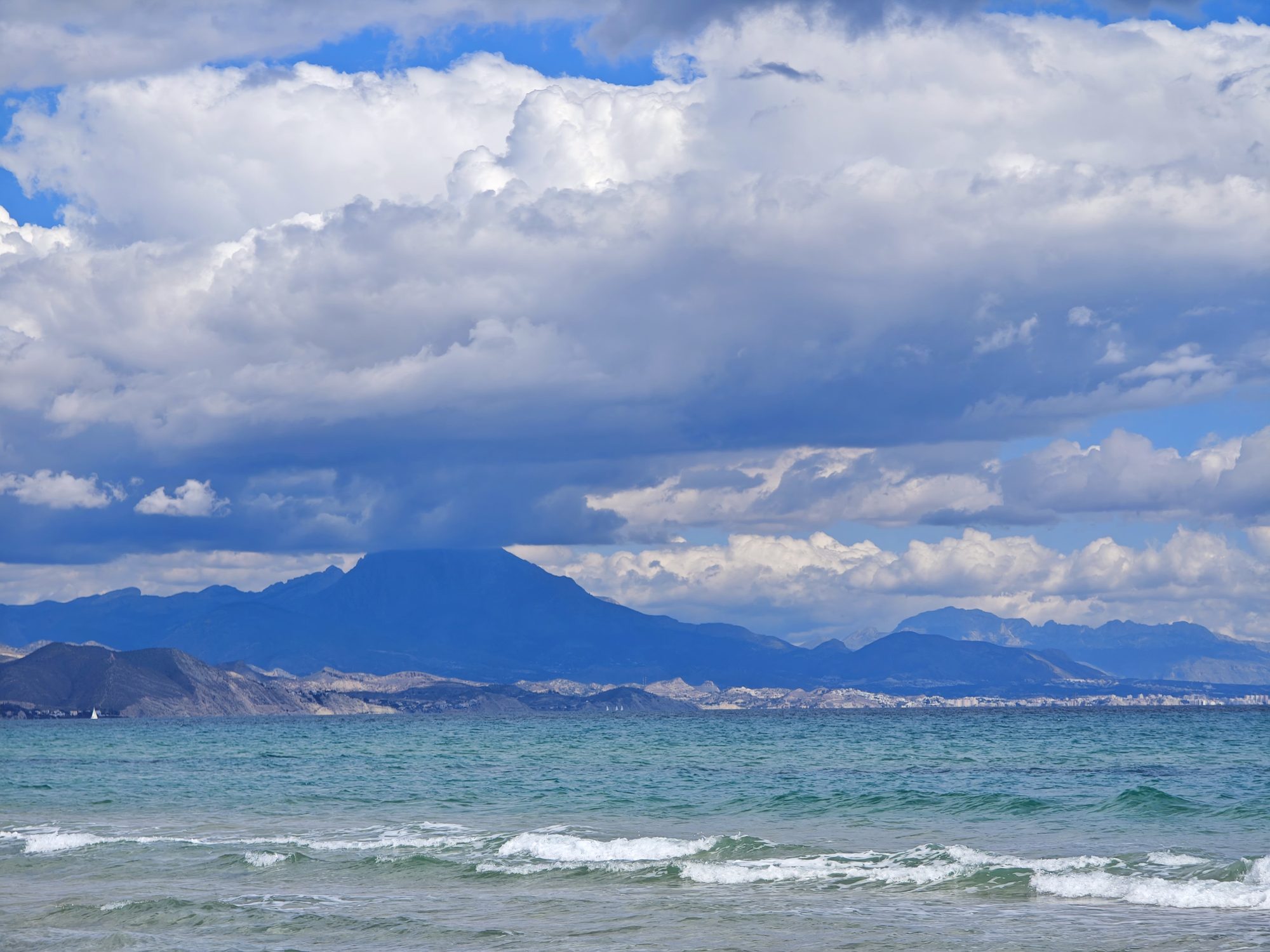 Vista del mar Mediterráneo y montañas alicantinas bajo un cielo de grandes nubes.