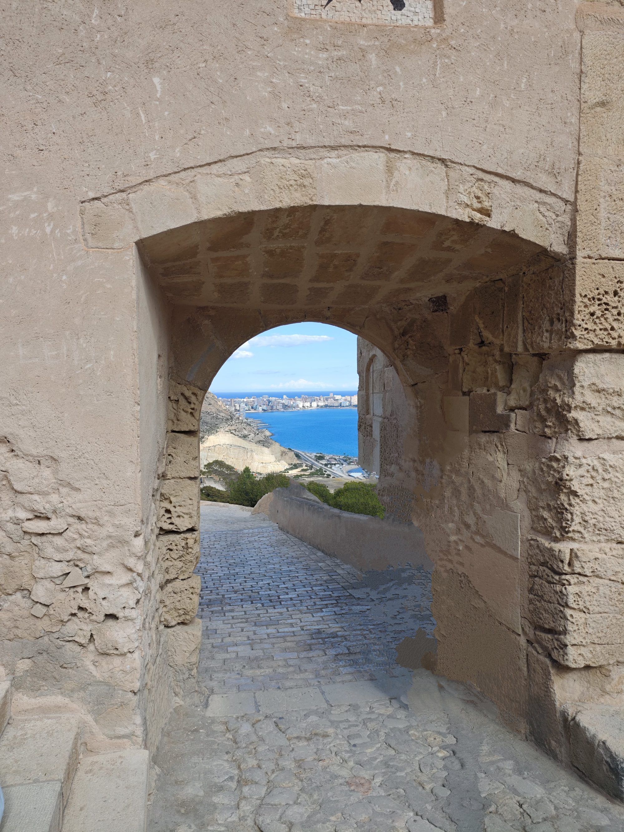 Arco de piedra antigua con vistas al mar azul y la costa de Alicante.
