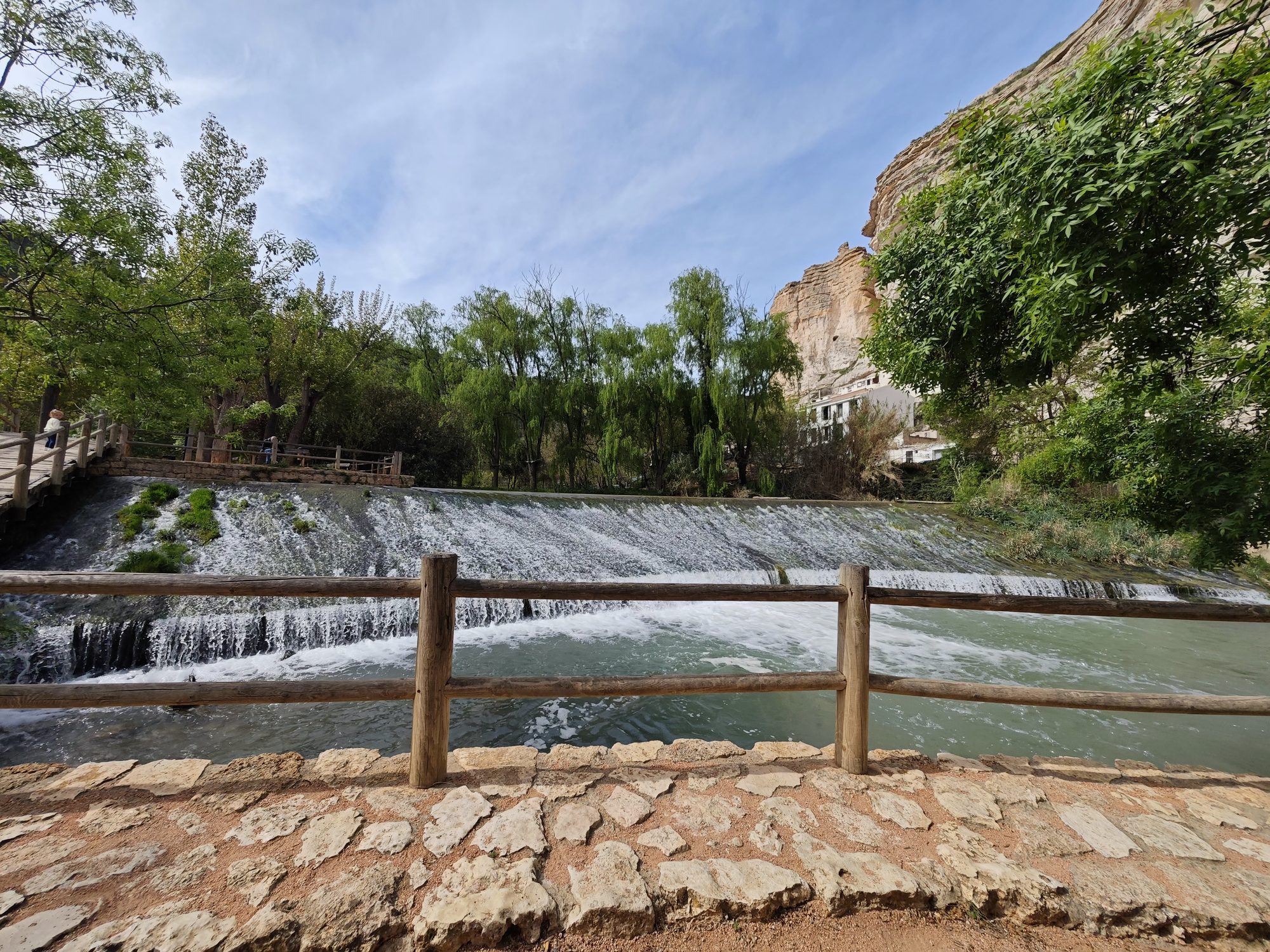 Cascada del río Júcar con valla de madera y acantilados rocosos al fondo.