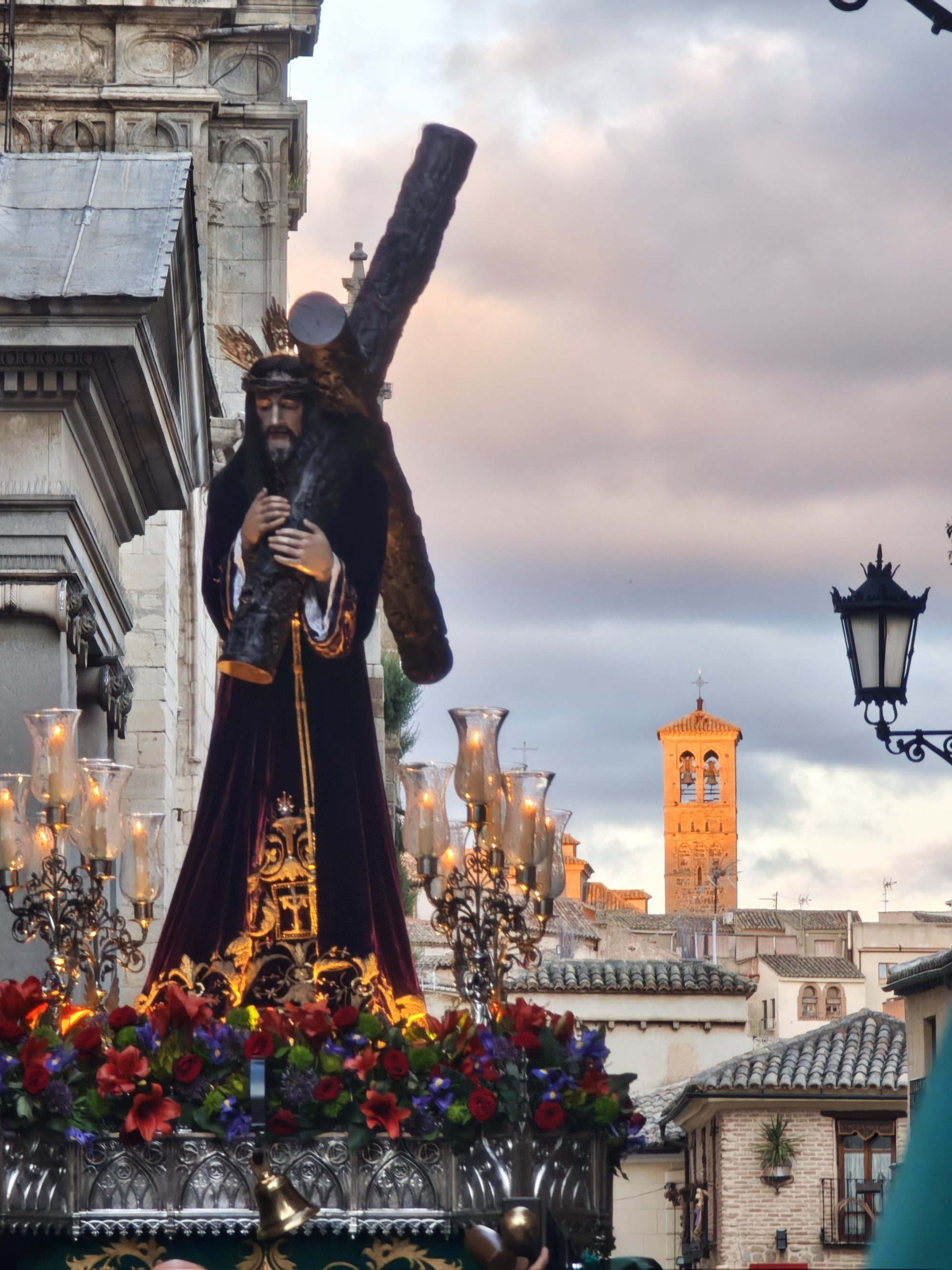 Paso procesional de Jesús con la cruz recorriendo las calles históricas de Toledo al atardecer.