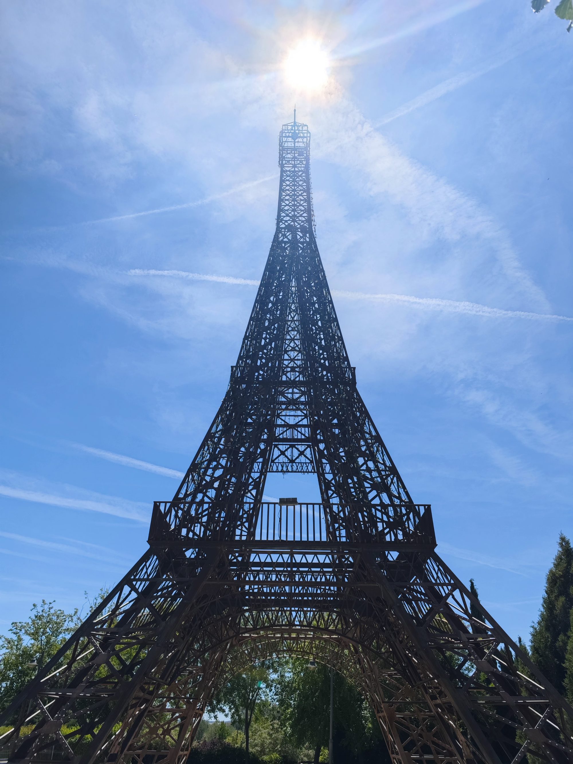 Réplica metálica de la Torre Eiffel vista en contrapicado bajo un sol brillante.