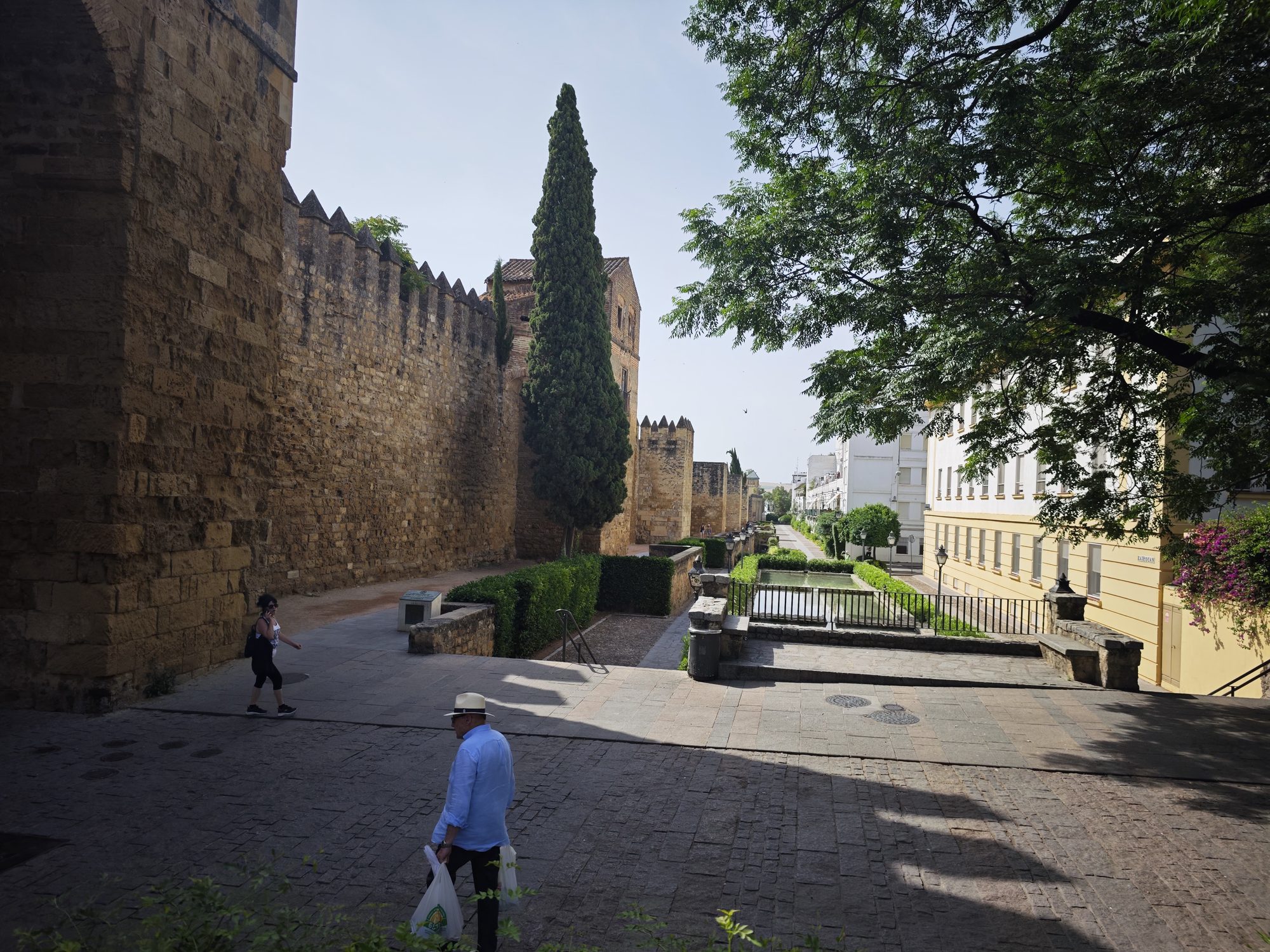 Murallas históricas de piedra con almenas y cipreses junto a un paseo en Córdoba.