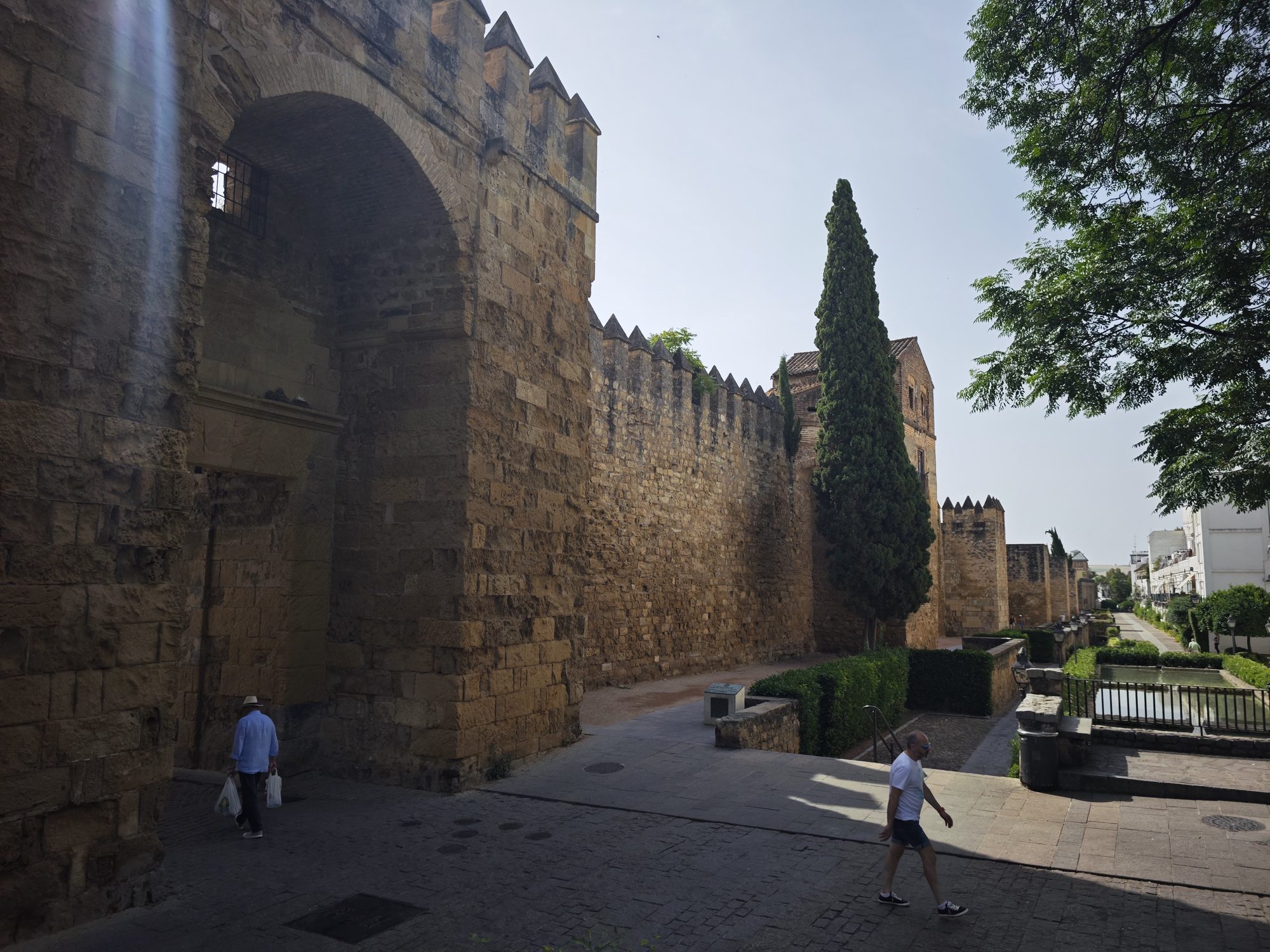 Muralla medieval de piedra con almenas y arco junto a un ciprés en Córdoba.