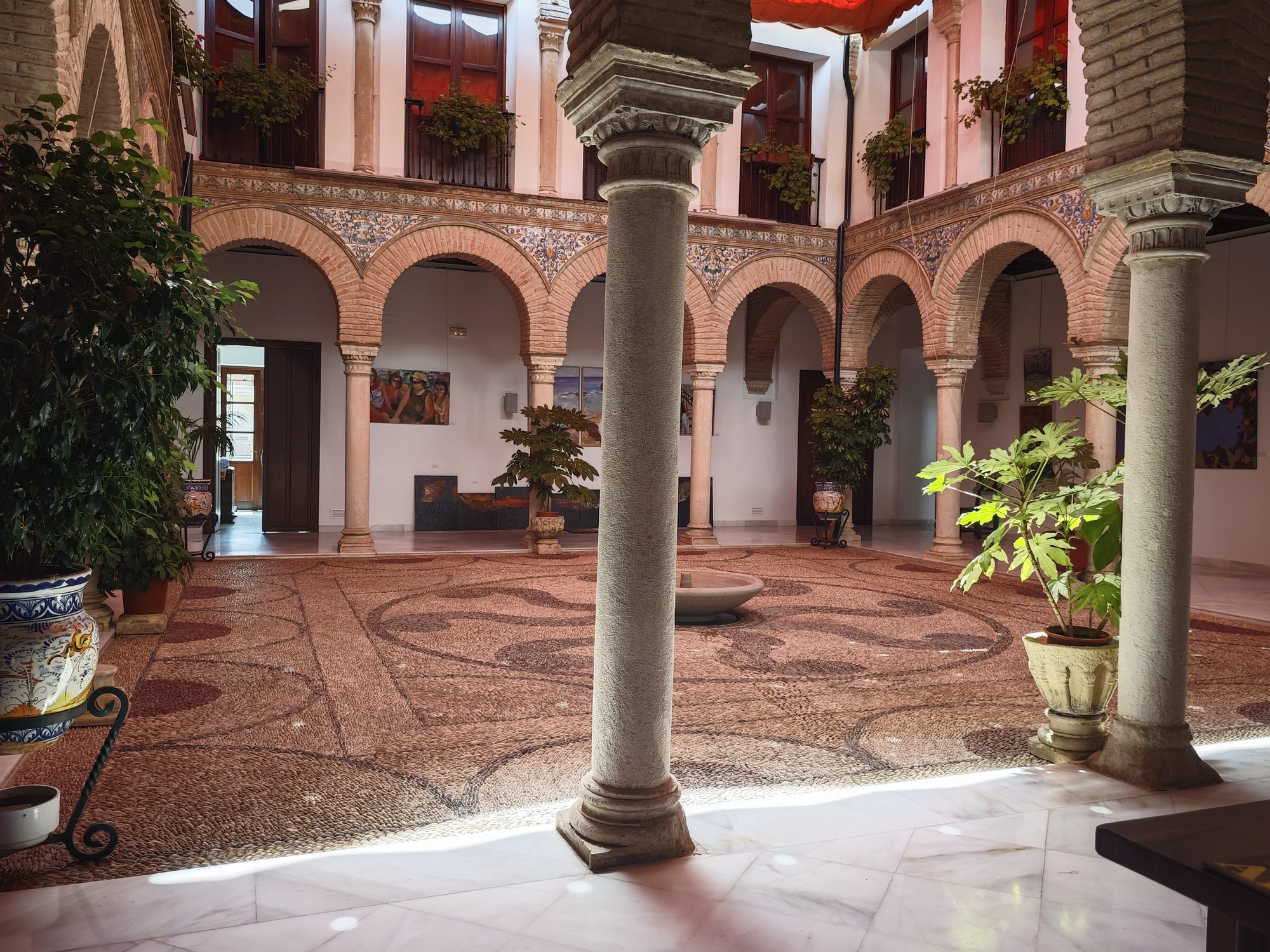 Patio tradicional andaluz con arcos de ladrillo, columnas de piedra, suelo empedrado y plantas.