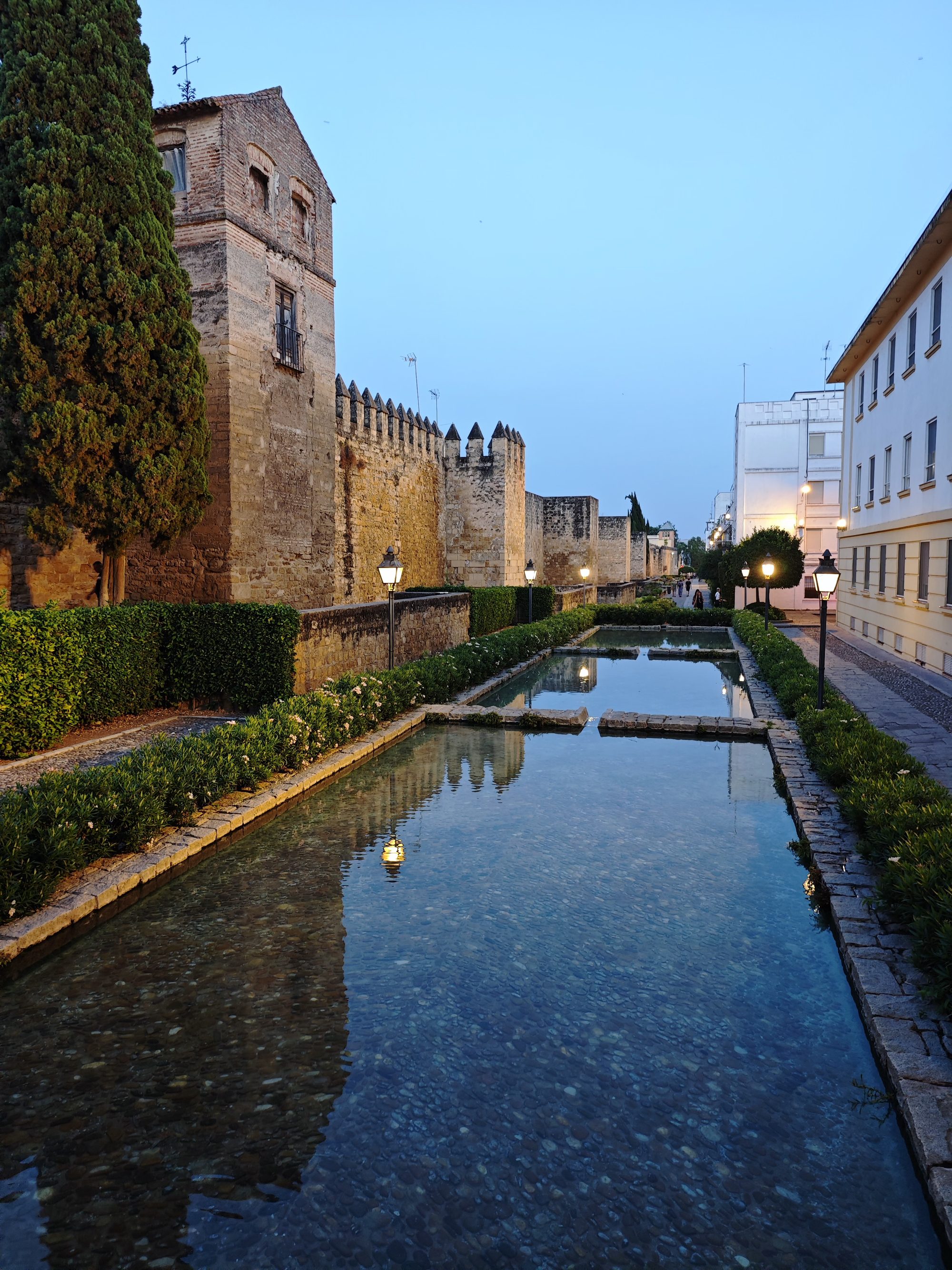 Estanque con reflejos junto a la muralla medieval iluminada de Córdoba al atardecer.