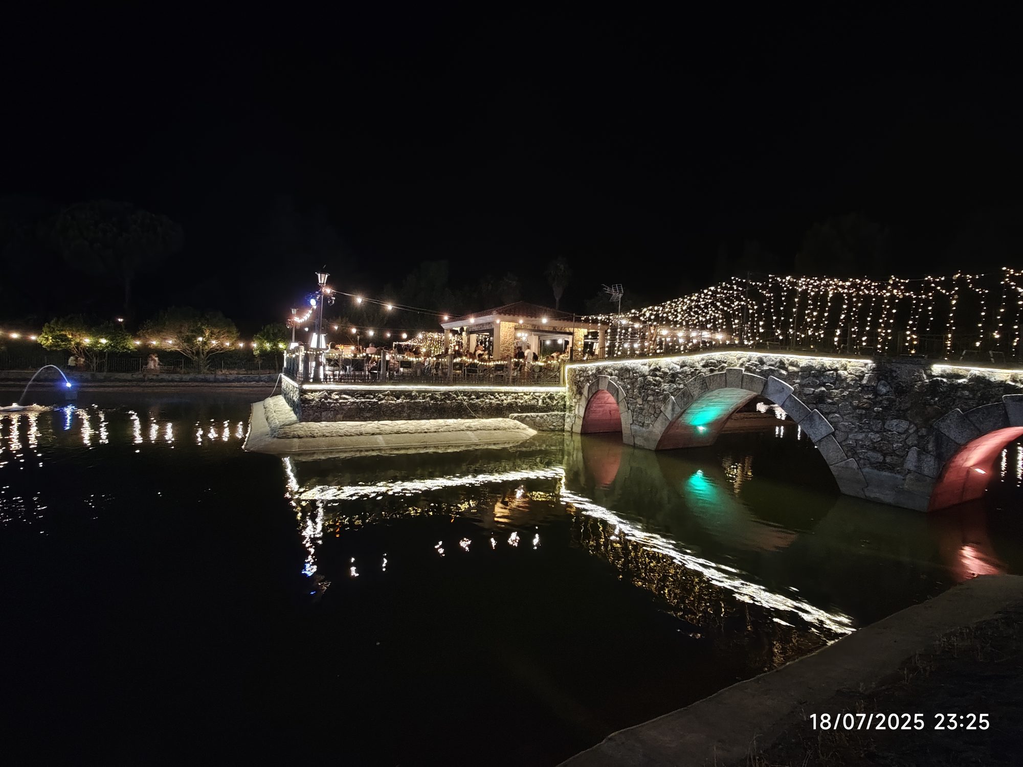 Puente de piedra iluminado con luces festivas reflejándose en el agua por la noche.