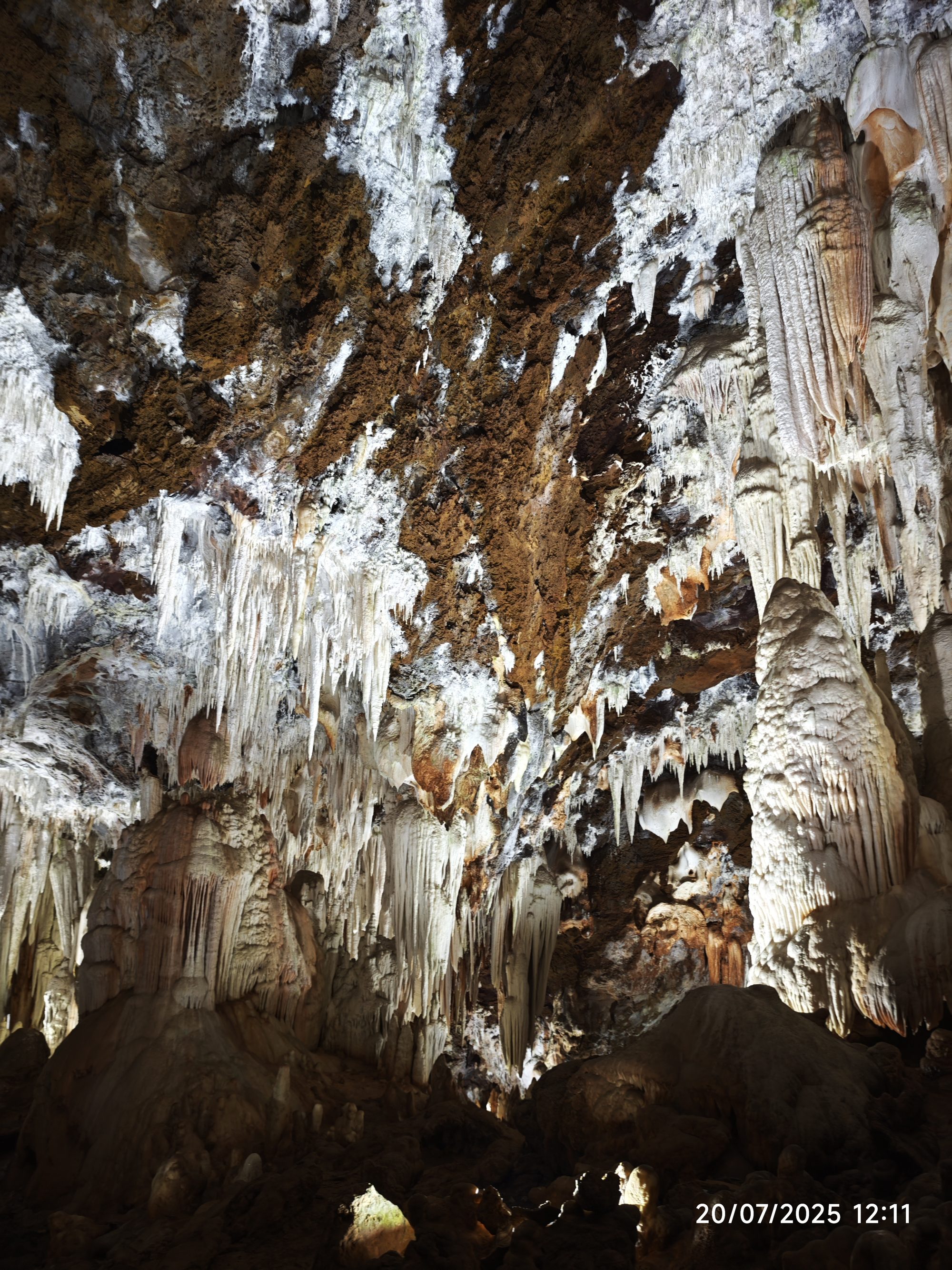 Formaciones de estalactitas y estalagmitas iluminadas en el techo y paredes de una cueva subterránea.