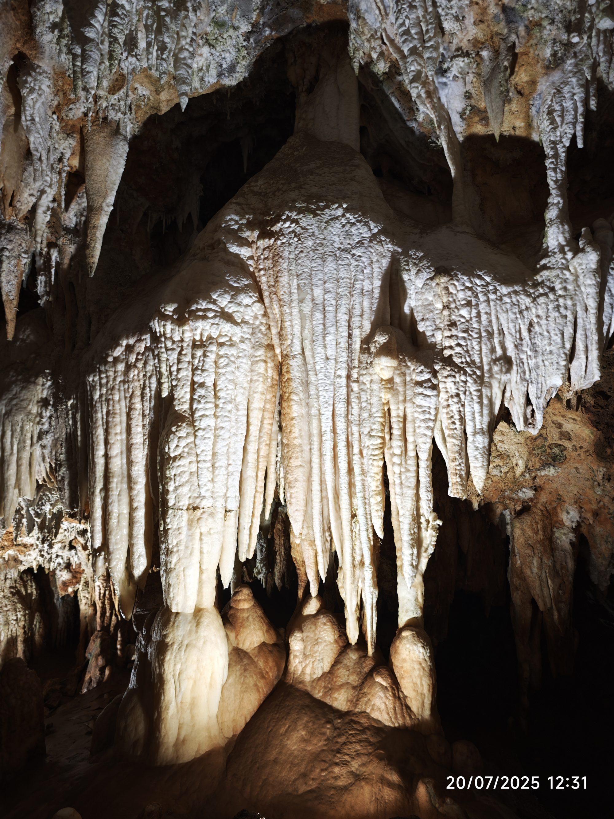 Grandes formaciones de estalactitas y estalagmitas iluminadas en el interior de una cueva subterránea.