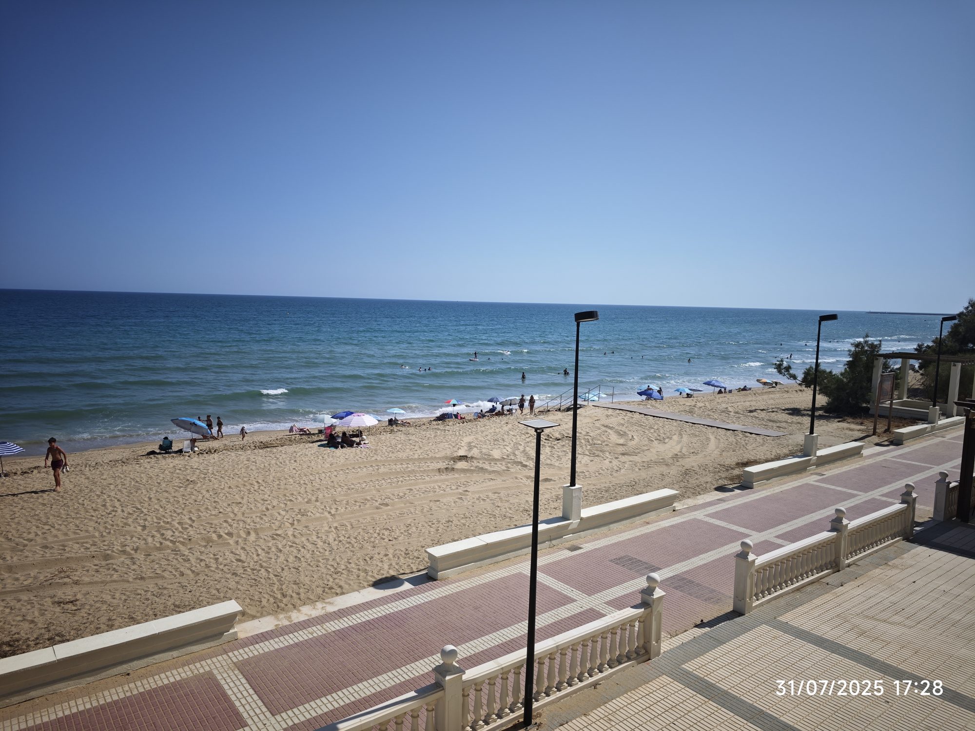 Paseo marítimo con balaustrada mirando hacia la playa dorada y el mar azul.