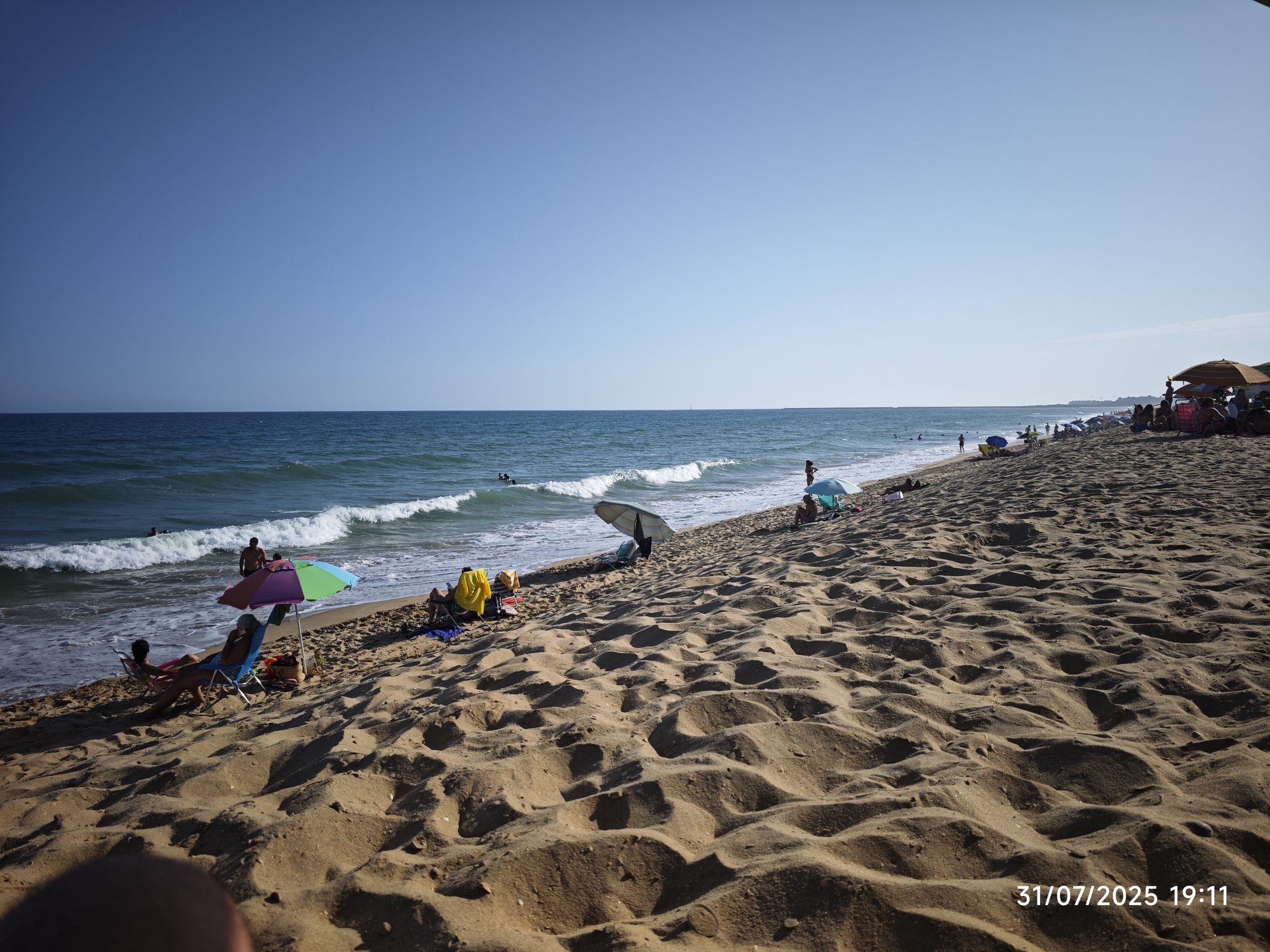 Playa de arena dorada con sombrillas frente al mar azul y cielo despejado.