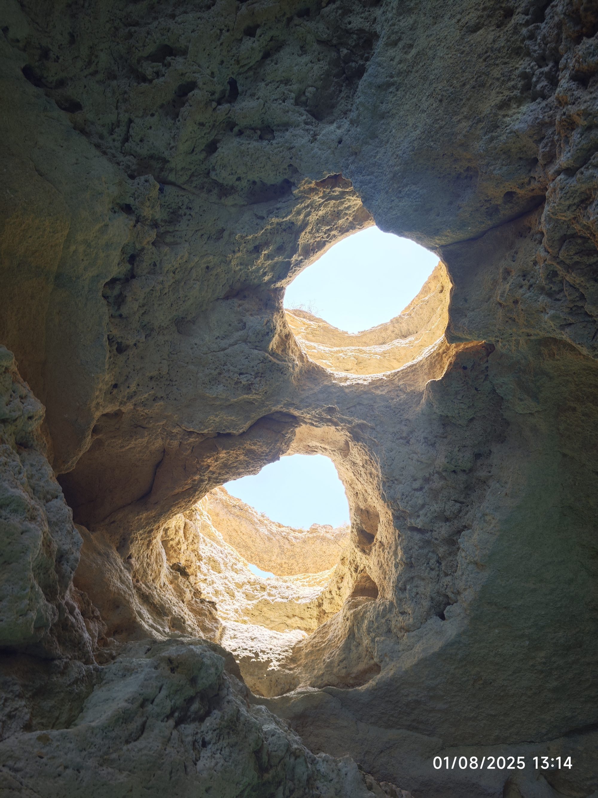 Aberturas naturales en el techo de roca de una cueva marina hacia el cielo azul.