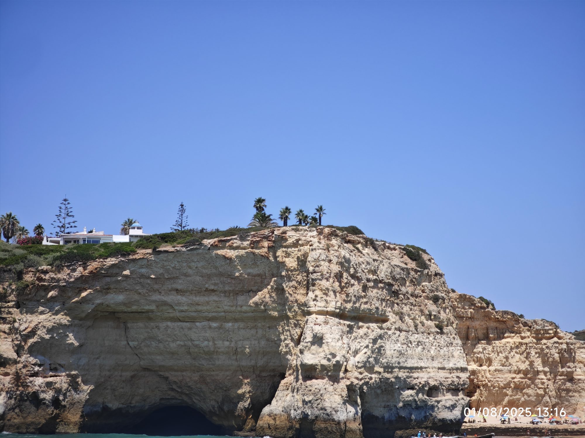 Acantilados dorados de piedra caliza con cueva marina y palmeras bajo un cielo azul.