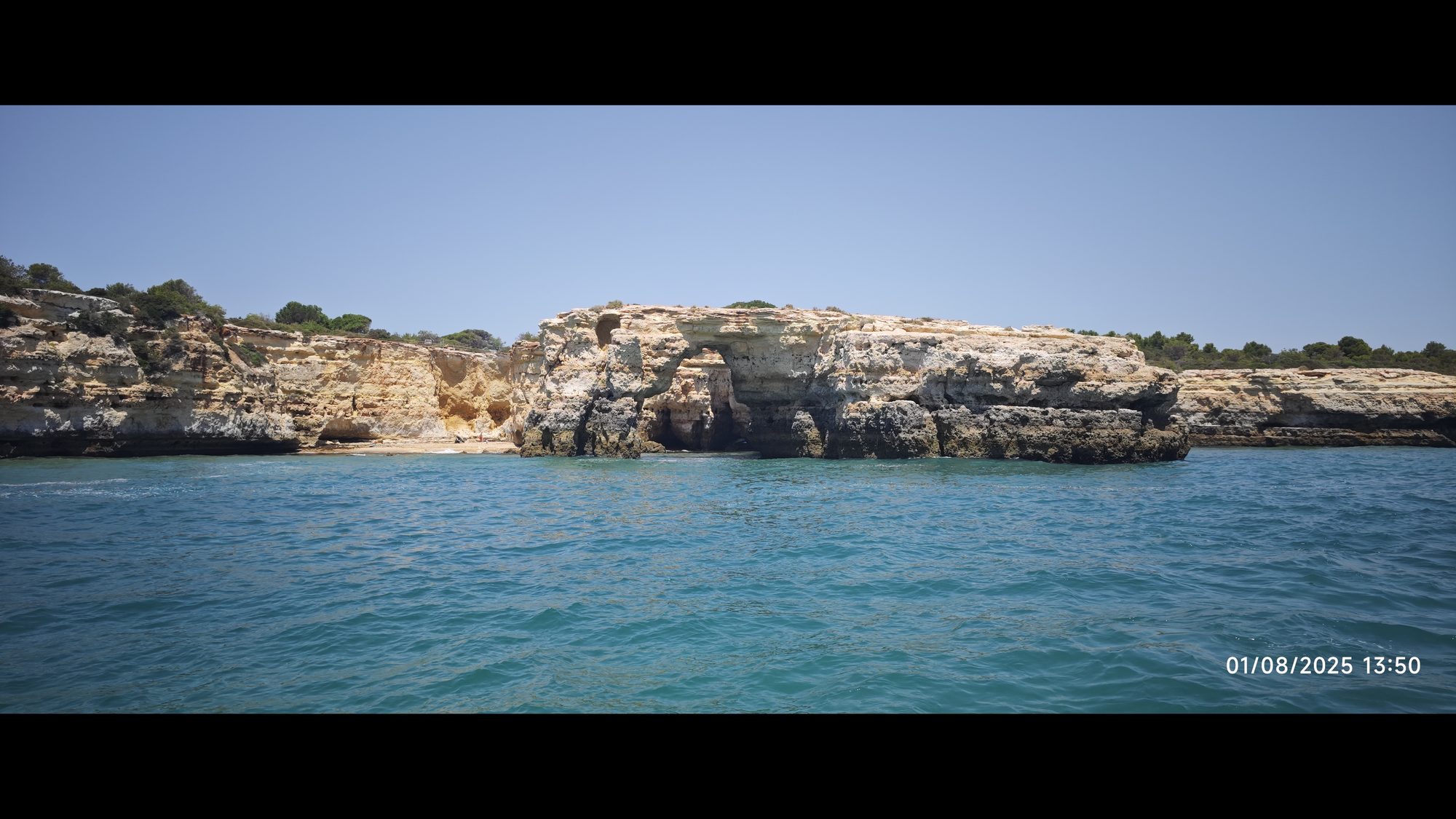 Acantilados dorados y un arco natural de roca sobre el agua turquesa del mar.