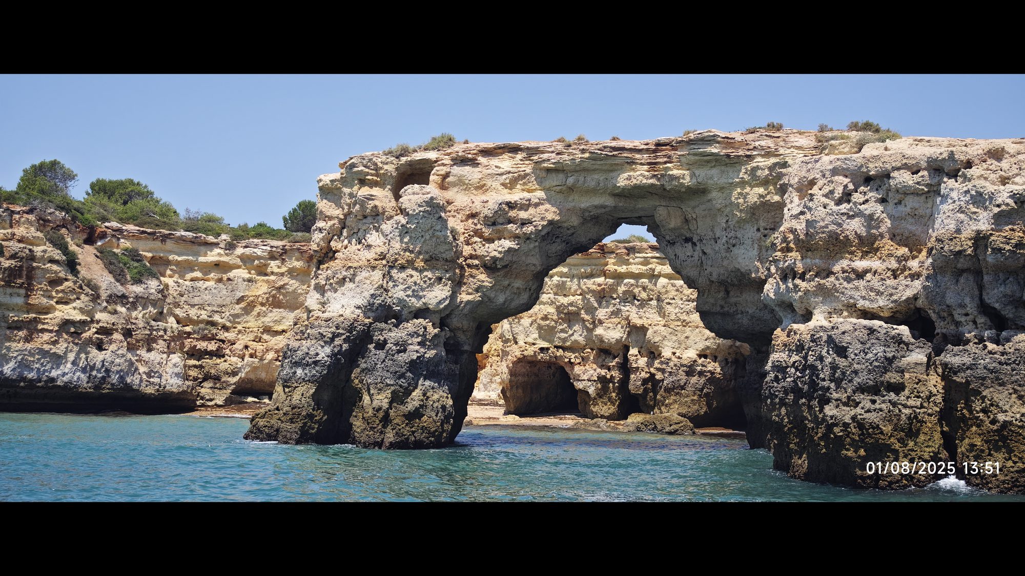 Impresionante arco de piedra natural y acantilados dorados sobre el mar turquesa.