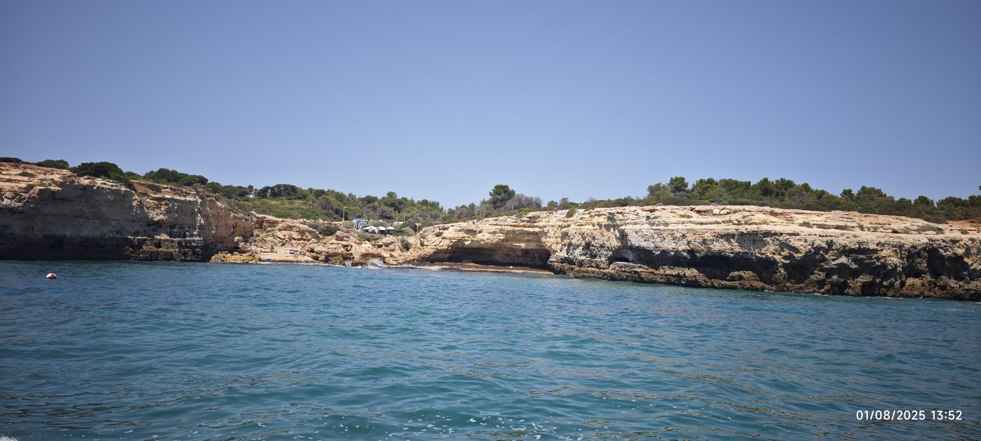 Acantilados dorados y cueva marina junto al mar turquesa bajo un cielo despejado.