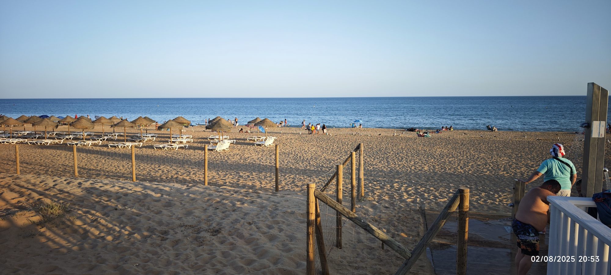Playa de arena dorada con sombrillas de paja y el mar bajo un cielo despejado.