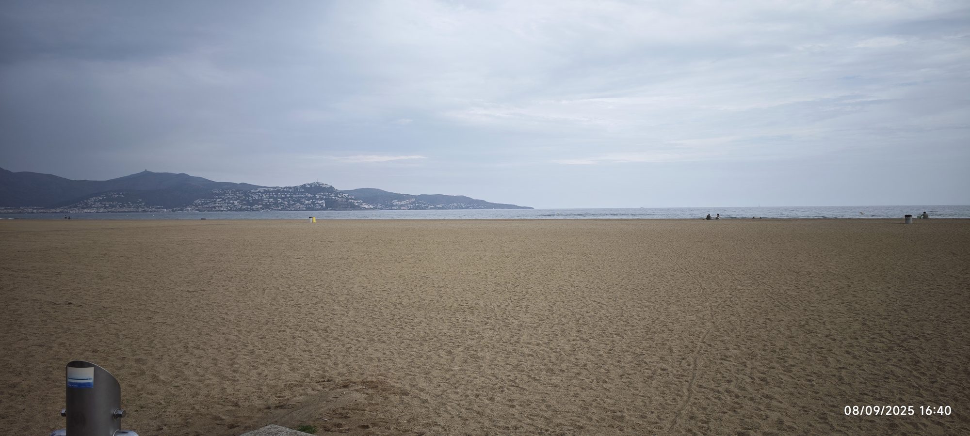 Amplia playa de arena dorada con el mar y colinas costeras bajo un cielo nublado.