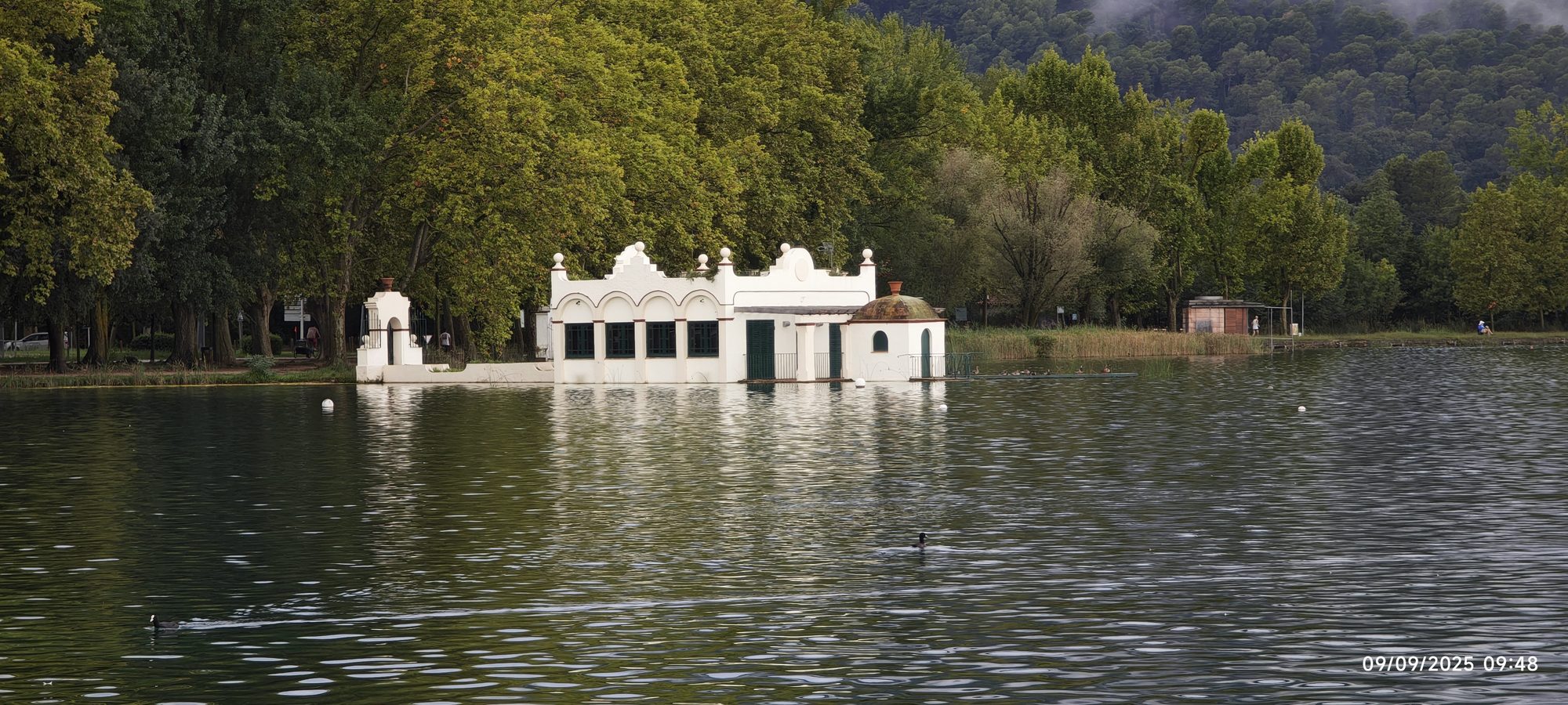 Pesquera blanca tradicional a orillas del tranquilo lago de Banyoles rodeada de frondosa vegetación.