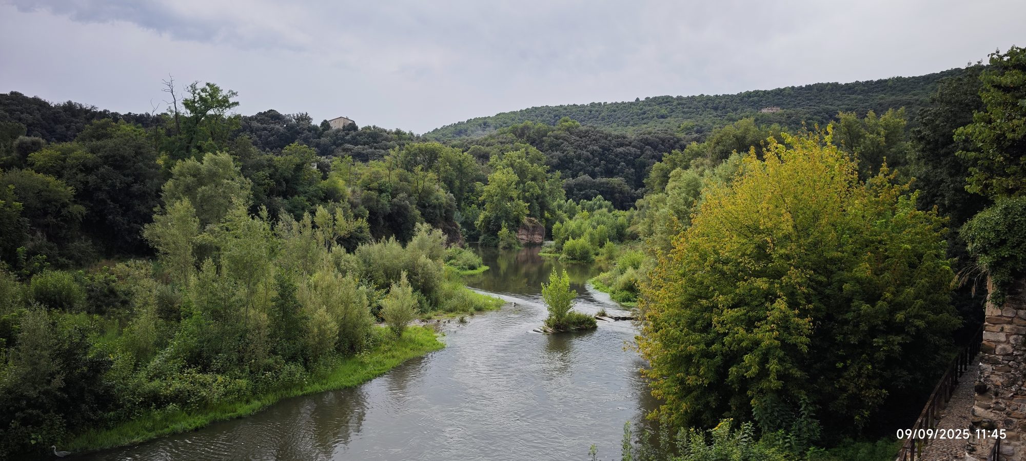 Río fluyendo entre vegetación frondosa y colinas arboladas bajo un cielo nublado.