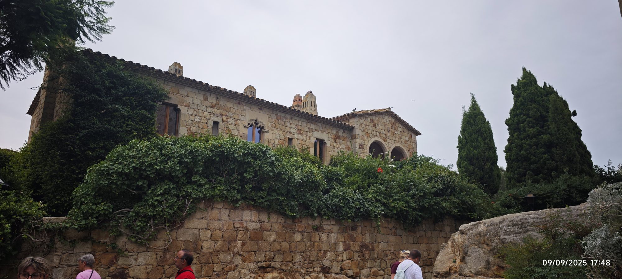 Edificio medieval de piedra rodeado de frondosa vegetación y cipreses en Pals.
