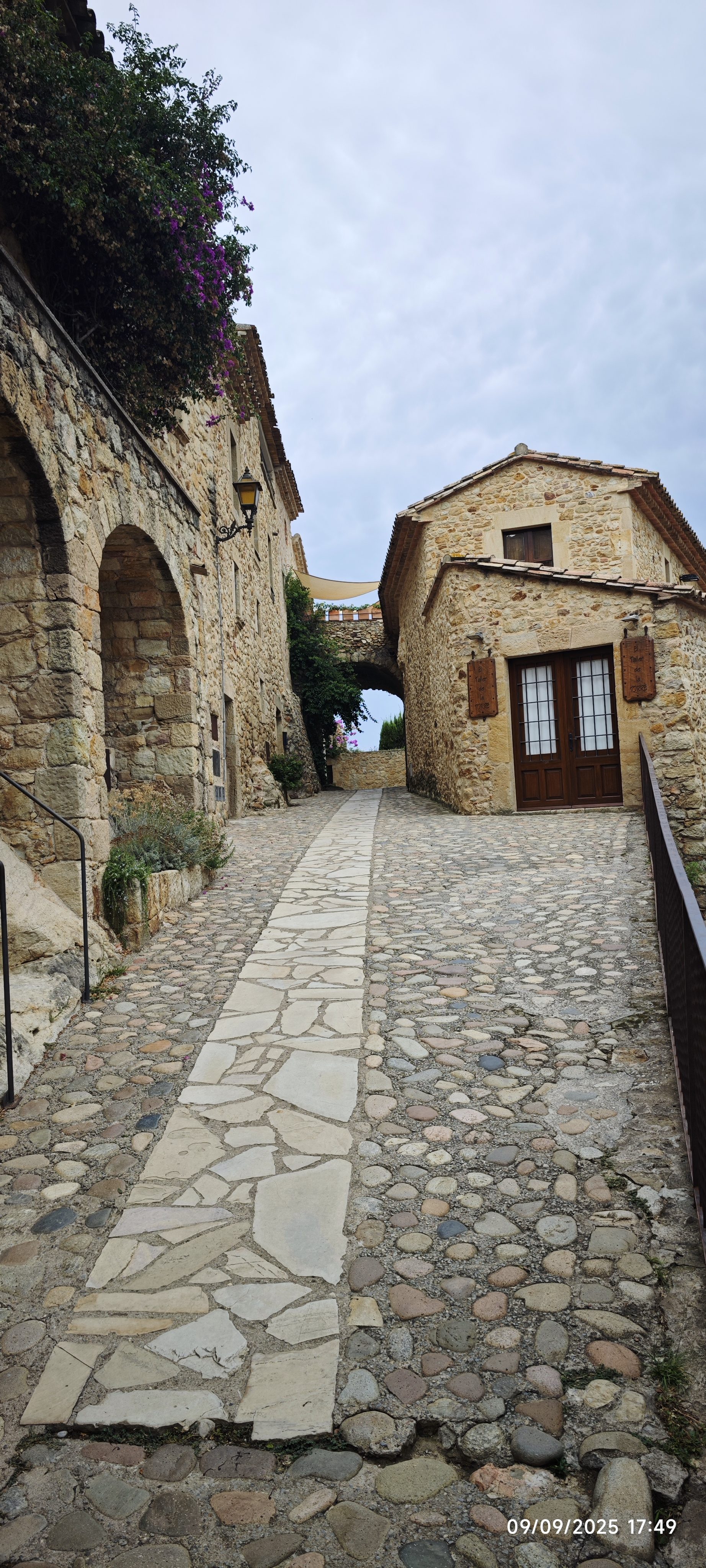 Calle empedrada entre casas medievales de piedra con arcos y plantas en Pals.