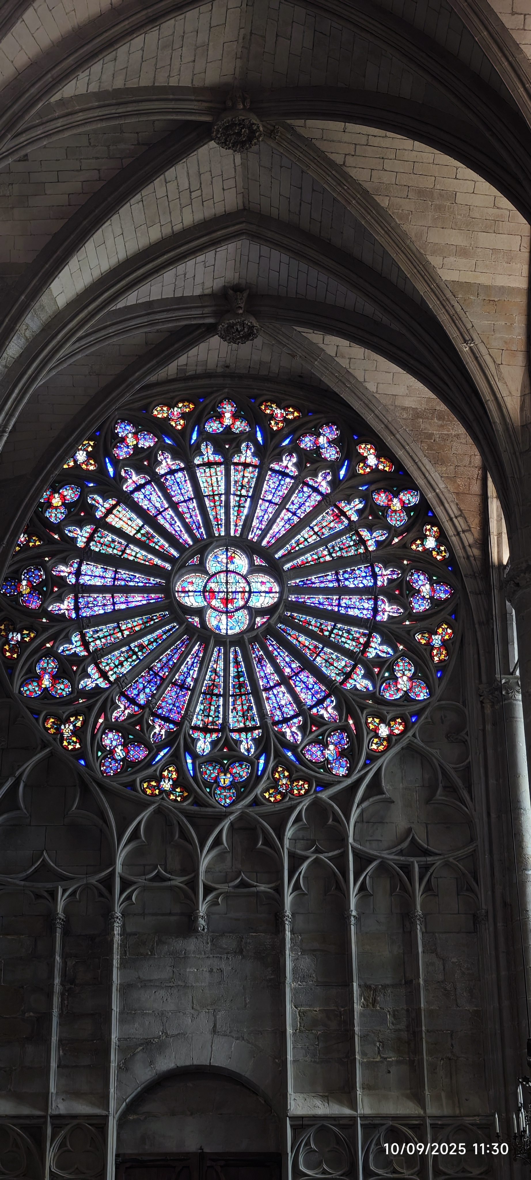 Rosetón gótico con vidrieras de colores en el interior de piedra de una basílica.